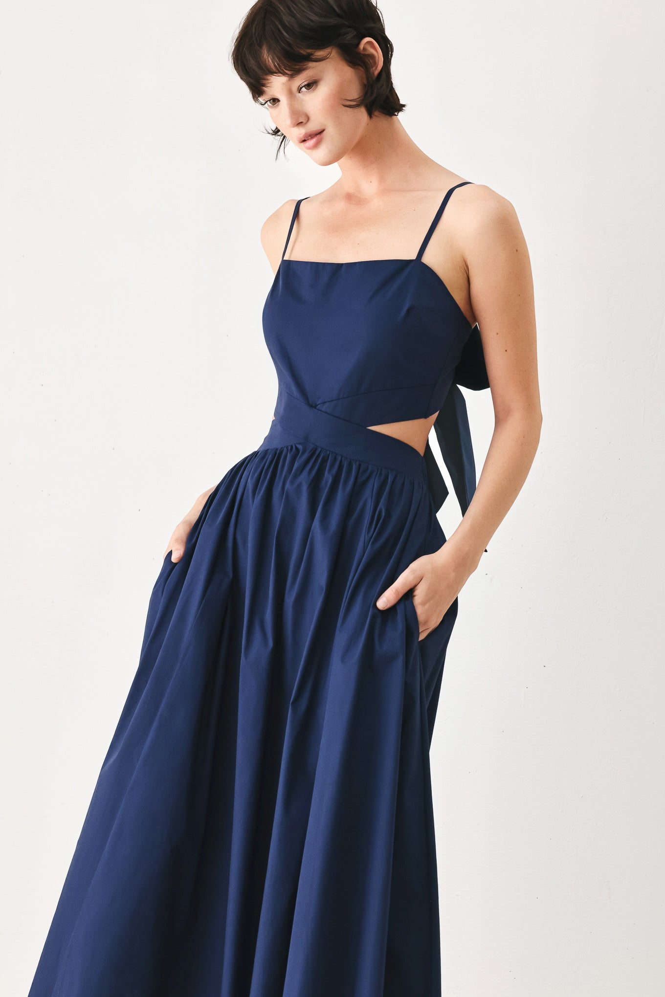 Woman wearing a navy midi dress featuring straight neckline, straps, waist cutout, full skirt, and tie detail | FREEMARKET