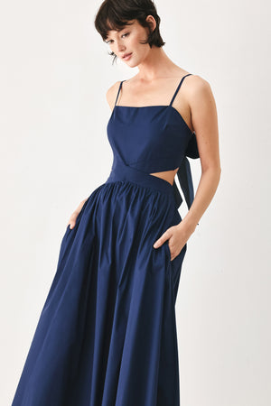 Woman wearing a navy midi dress featuring straight neckline, straps, waist cutout, full skirt, and tie detail | FREEMARKET