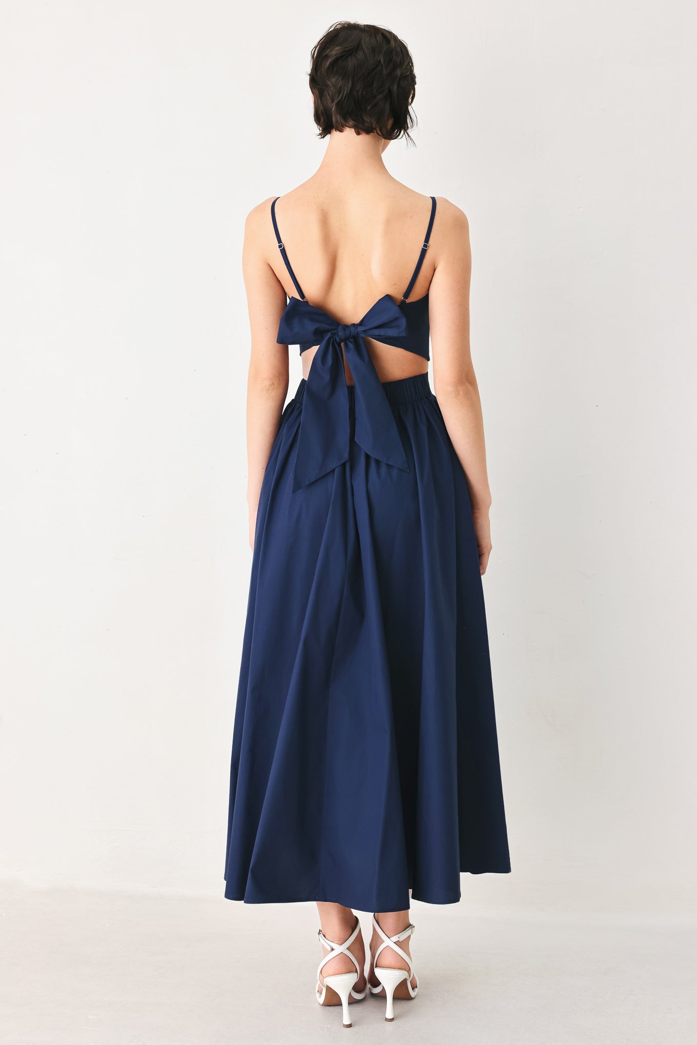 Woman wearing a navy midi dress featuring straight neckline, straps, waist cutout, full skirt, and tie detail | FREEMARKET
