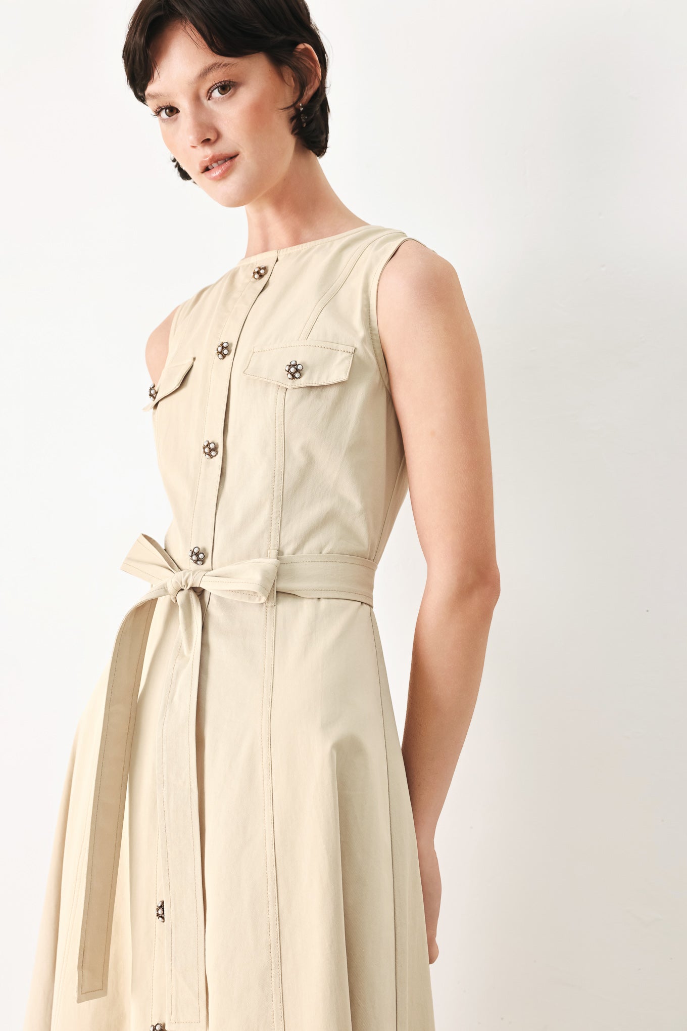 Woman wearing a beige khaki sleeveless midi dress with round neckline, front button detail, self sash tie, circle skirt and back zipper closure | FREEMARKET
