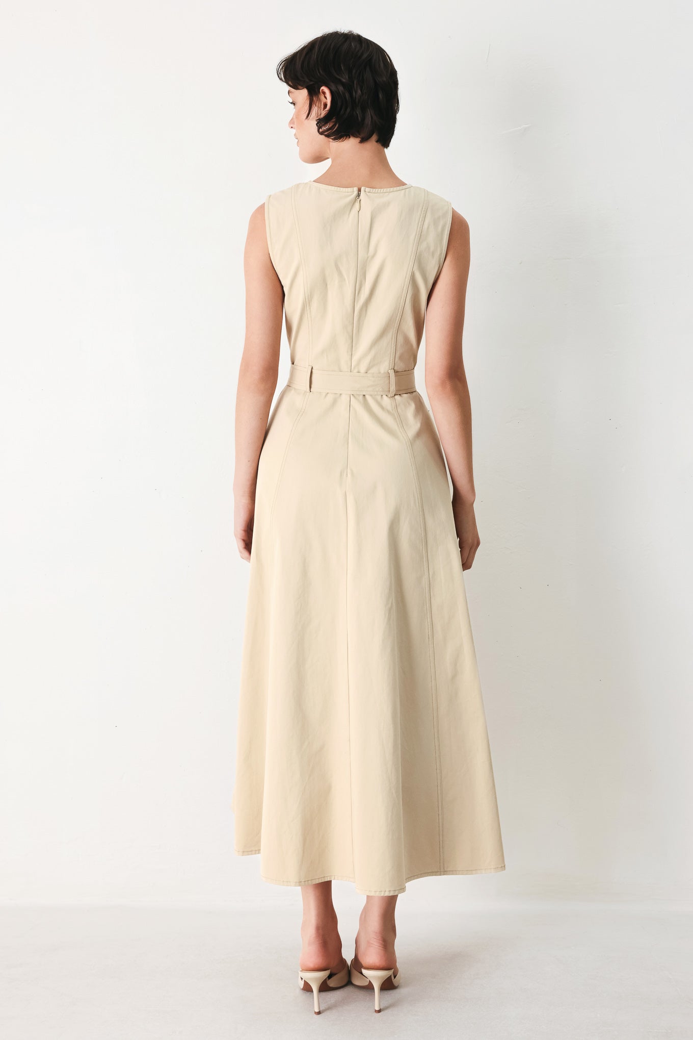Woman wearing a beige khaki sleeveless midi dress with round neckline, front button detail, self sash tie, circle skirt and back zipper closure | FREEMARKET