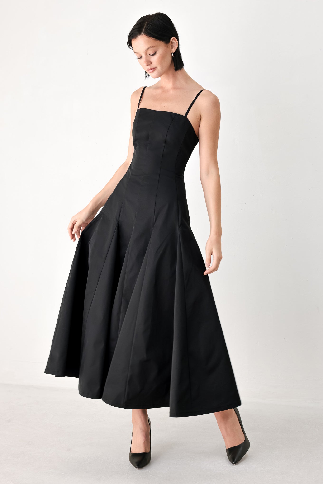 A woman modeling a black midi dress with thin spaghetti straps, a structured square neckline, and a flared skirt | FREEMARKET