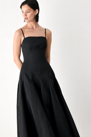 A woman modeling a black midi dress with thin spaghetti straps, a structured square neckline, and a flared skirt | FREEMARKET