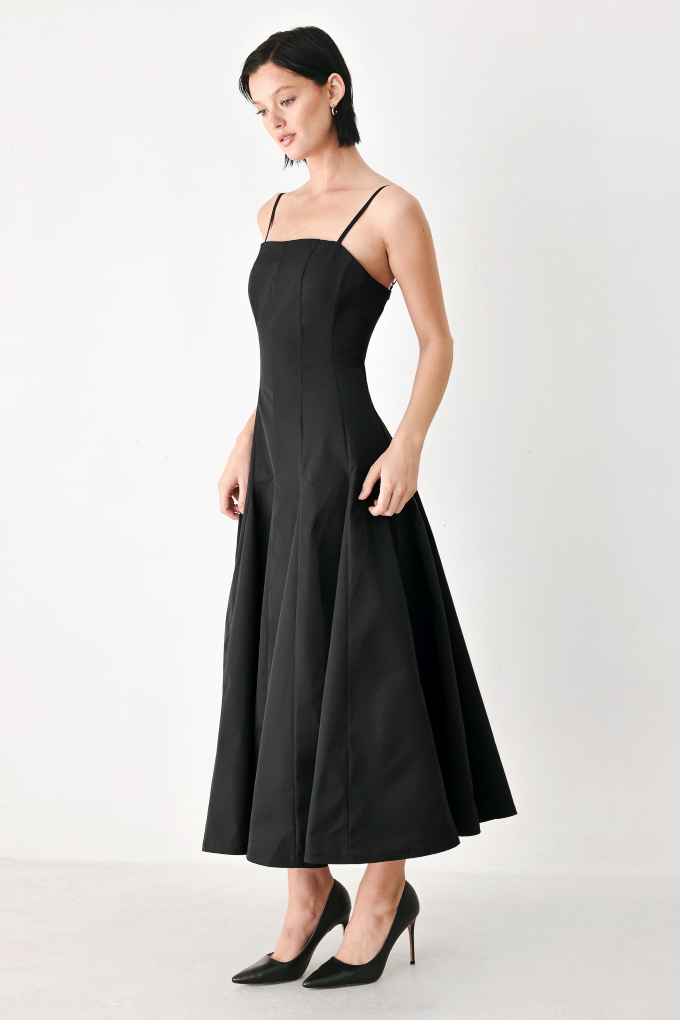 A woman modeling a black midi dress with thin spaghetti straps, a structured square neckline, and a flared skirt | FREEMARKET