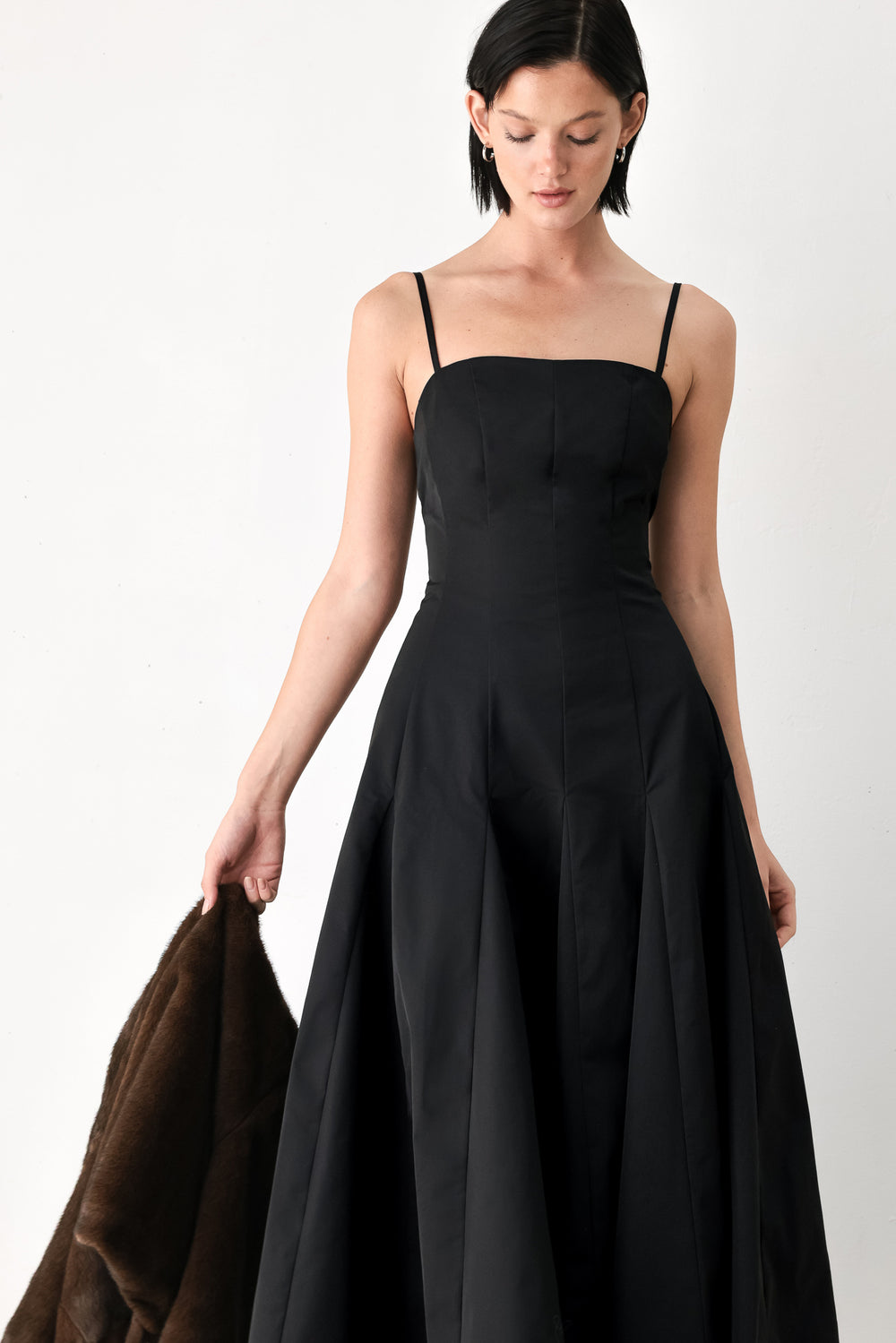 A woman modeling a black midi dress with thin spaghetti straps, a structured square neckline, and a flared skirt | FREEMARKET