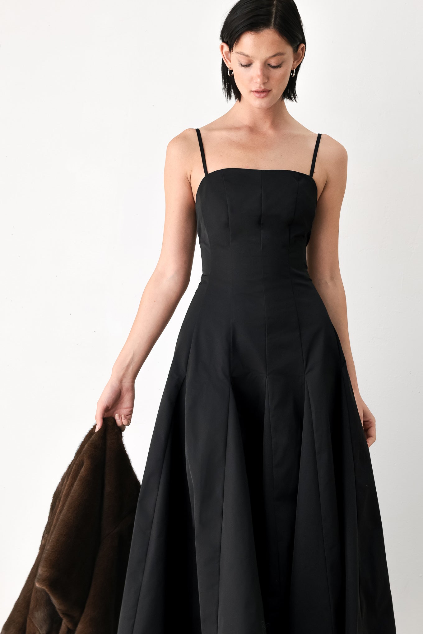 A woman modeling a black midi dress with thin spaghetti straps, a structured square neckline, and a flared skirt | FREEMARKET