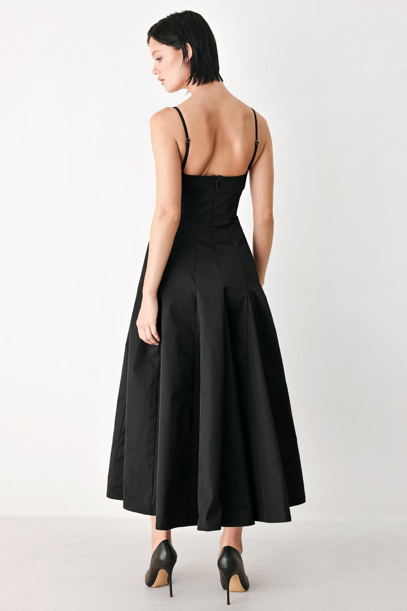 A woman modeling a black midi dress with thin spaghetti straps, a structured square neckline, and a flared skirt | FREEMARKET
