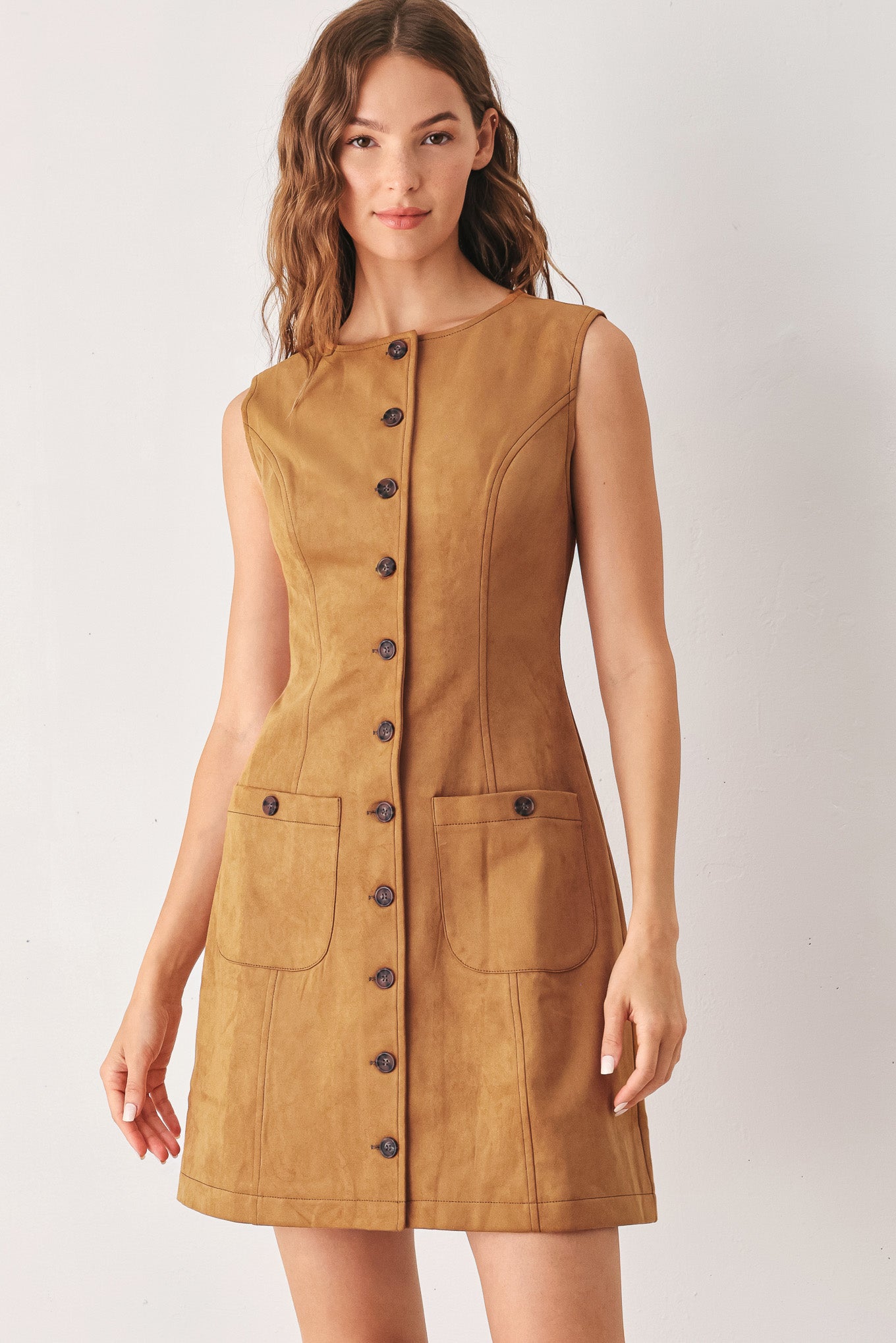 A woman wearing a sleeveless caramel dress with a front button placket and two front patch pockets | FREEMARKET