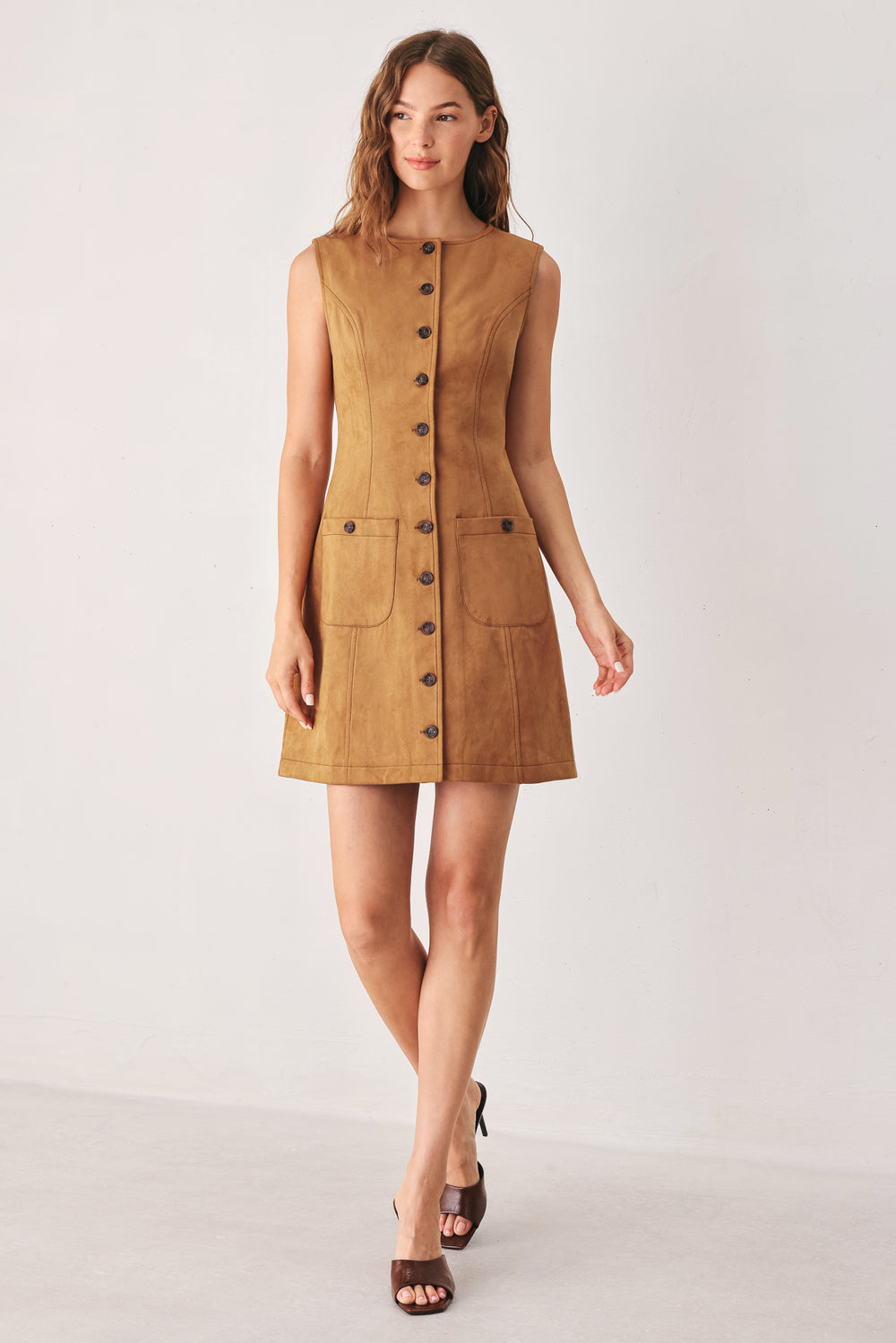 A woman wearing a sleeveless caramel dress with a front button placket and two front patch pockets | FREEMARKET