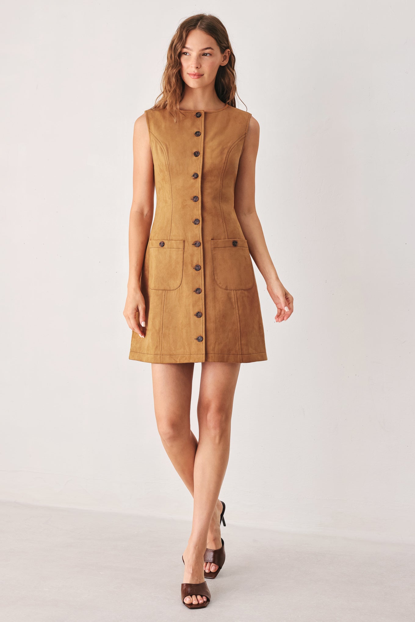 A woman wearing a sleeveless caramel dress with a front button placket and two front patch pockets | FREEMARKET