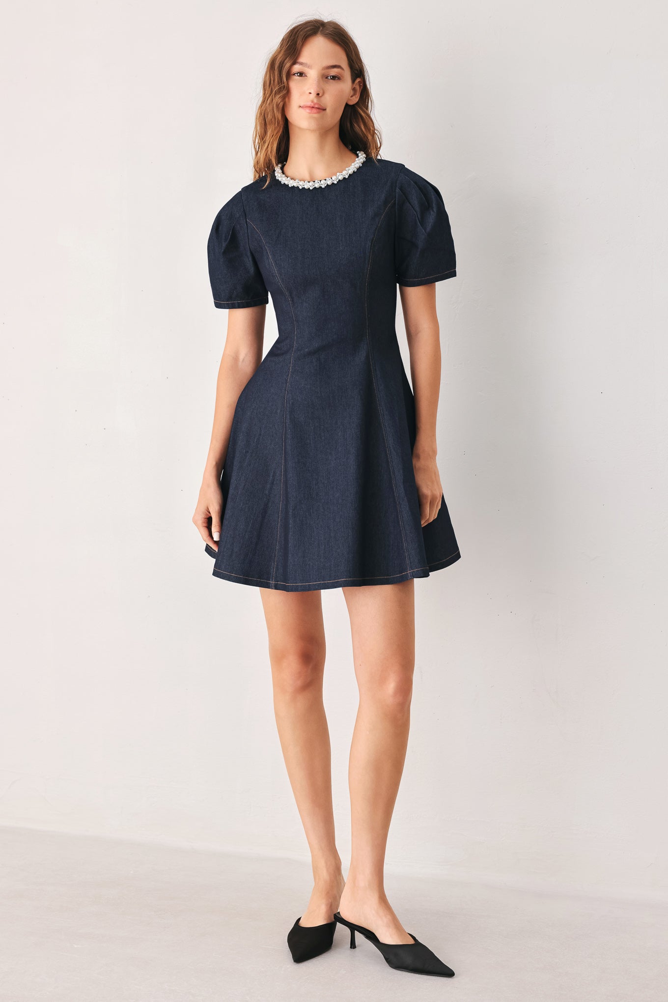 A woman wearing a dark navy blue mini dress with short puff sleeves, a round neckline accented with a white pearl collar, and a flared skirt | FREEMARKET