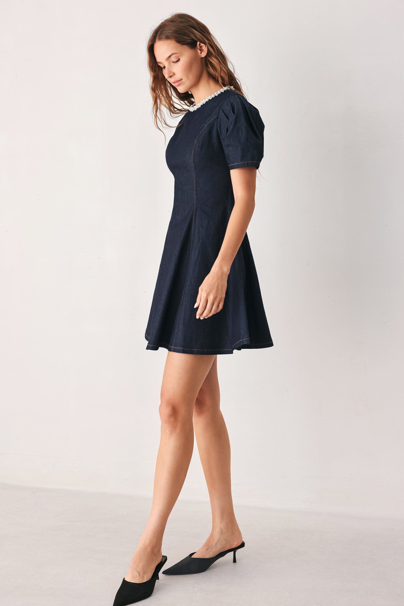 A woman wearing a dark navy blue mini dress with short puff sleeves, a round neckline accented with a white pearl collar, and a flared skirt | FREEMARKET