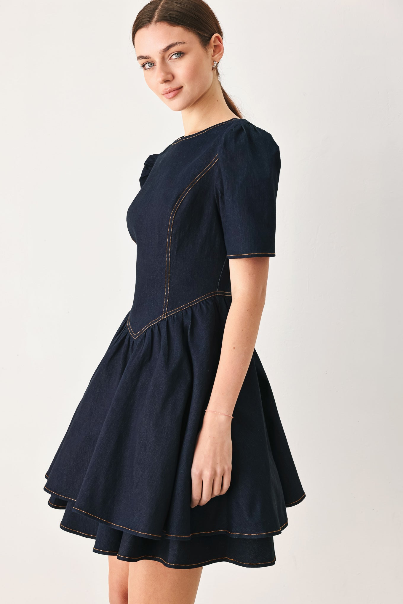 Woman wearing a dark denim navy blue mini dress featuring round neckline, short puff sleeve, basque waist, double layer skirt and back zipper closure | FREEMARKET
