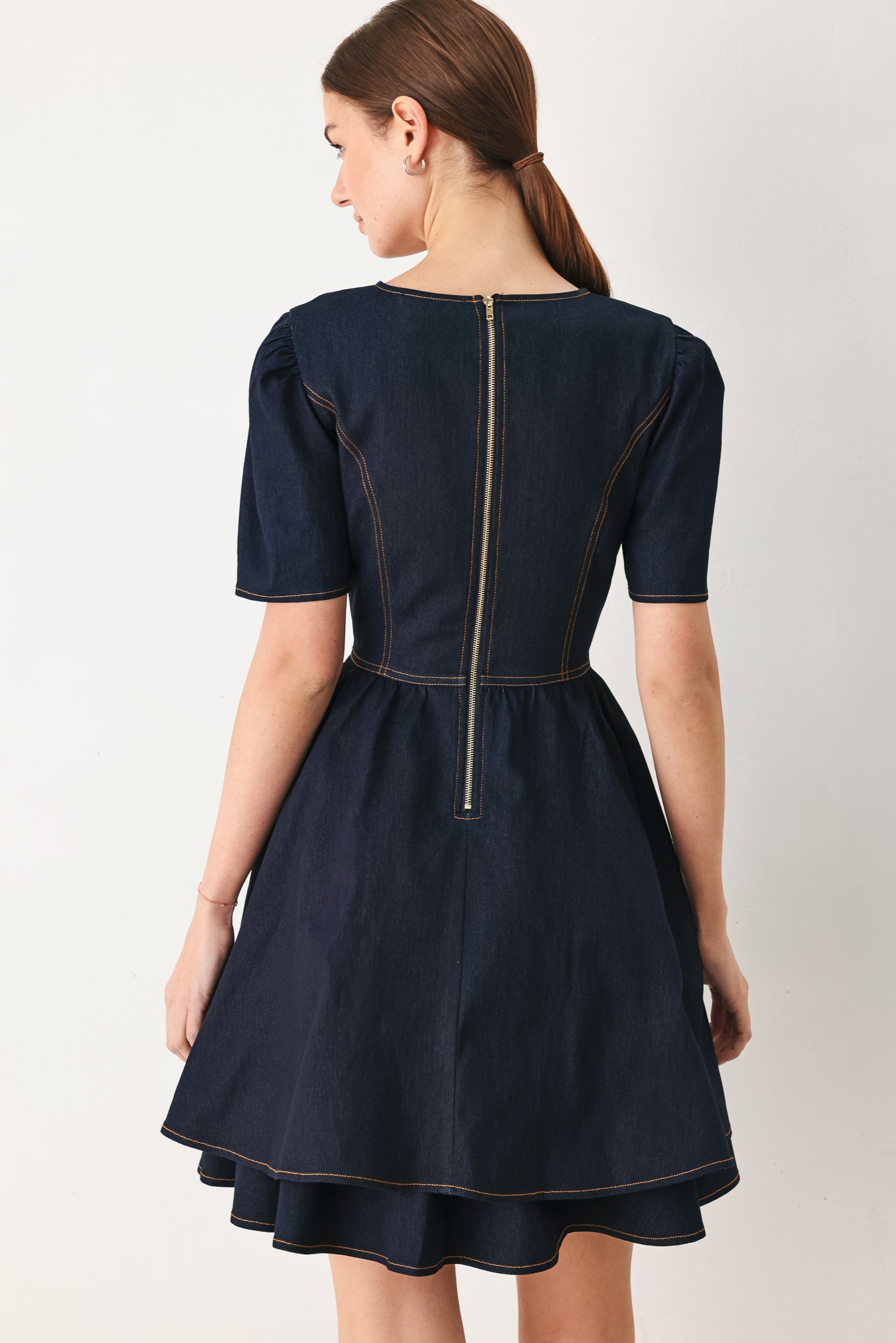 Woman wearing a dark denim navy blue mini dress featuring round neckline, short puff sleeve, basque waist, double layer skirt and back zipper closure | FREEMARKET