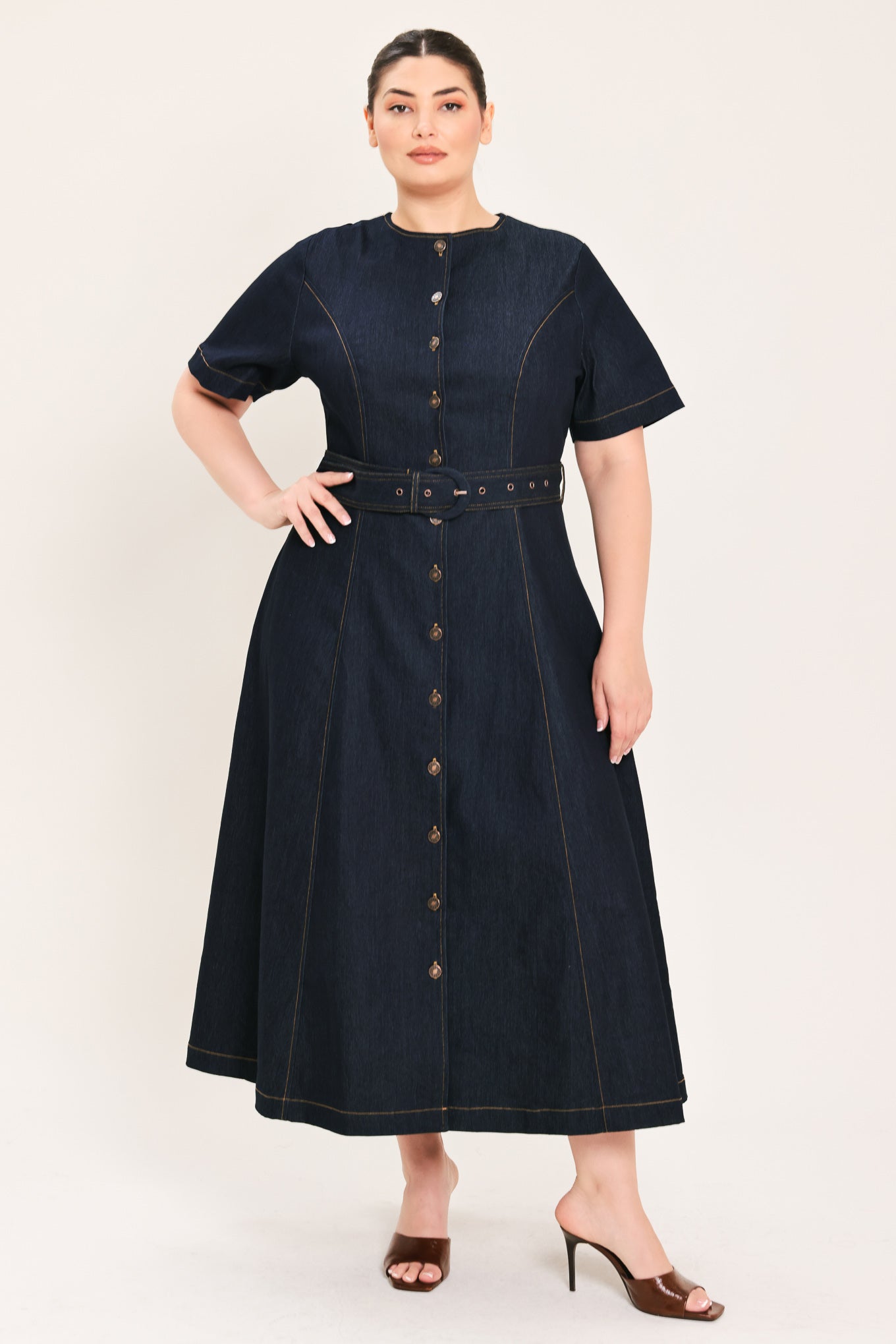 A woman modeling a dark indigo denim midi dress with short sleeves, a button-down front, and a matching belt with a metal buckle | Plus Curve Flying Tomato