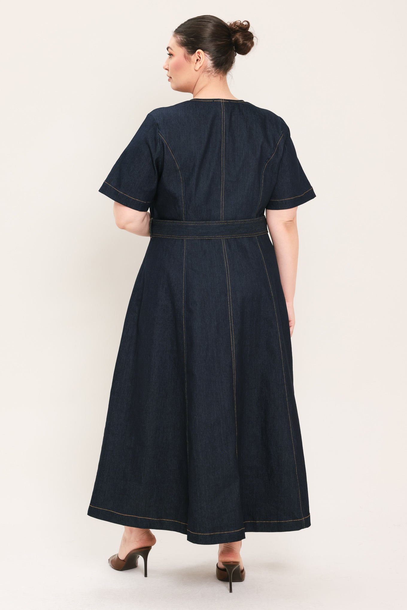 A woman modeling a dark indigo denim midi dress with short sleeves, a button-down front, and a matching belt with a metal buckle | Plus Curve Flying Tomato