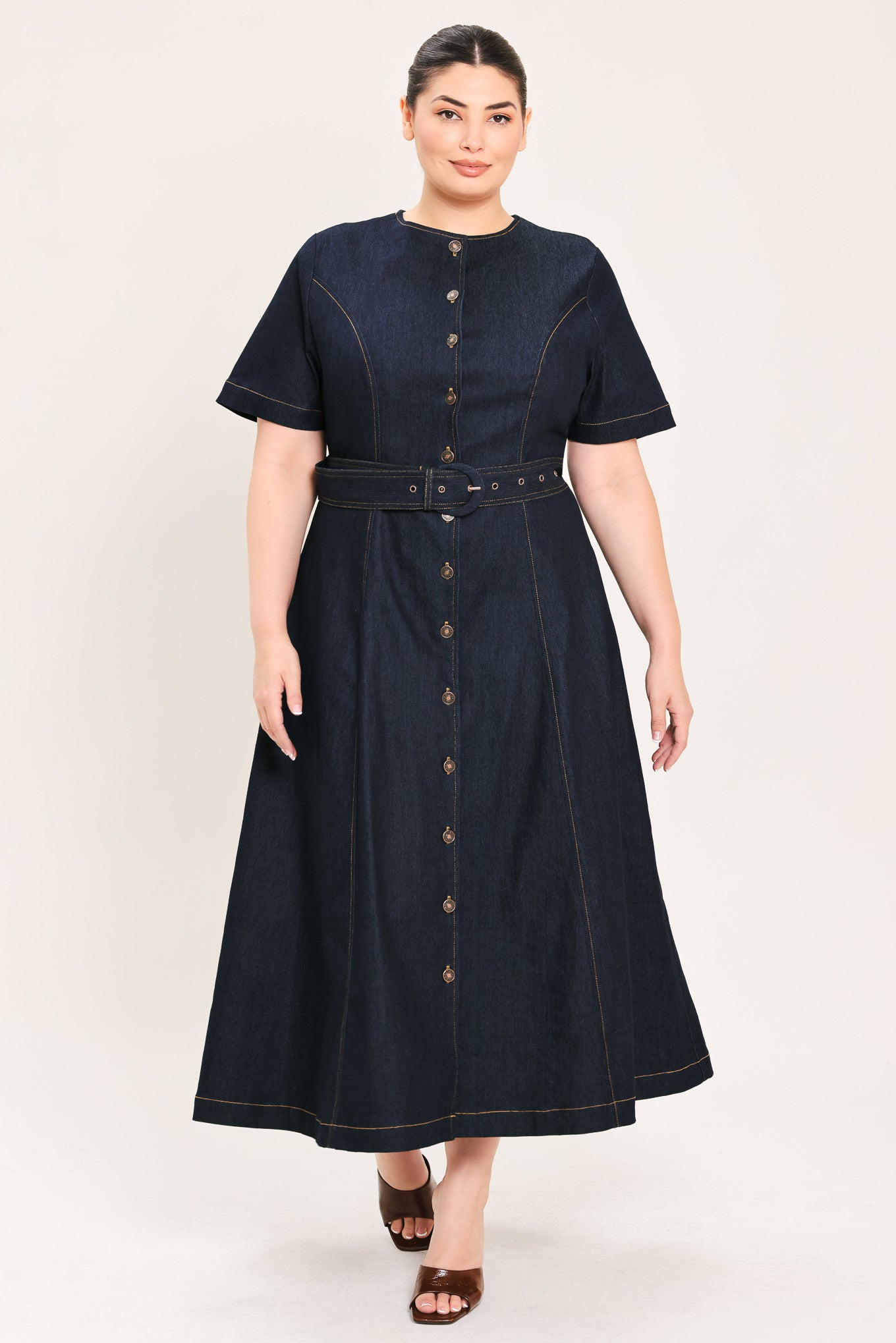 A woman modeling a dark indigo denim midi dress with short sleeves, a button-down front, and a matching belt with a metal buckle | Plus Curve Flying Tomato