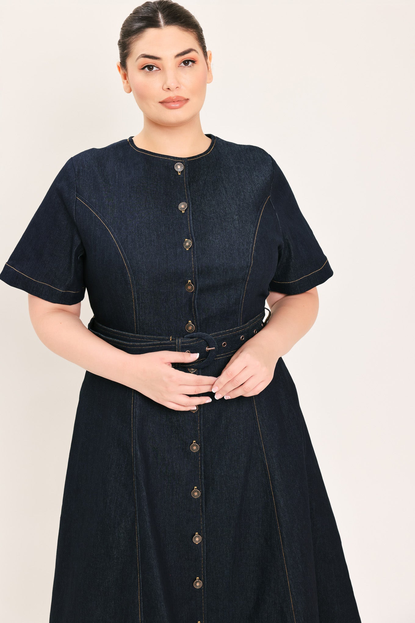 A woman modeling a dark indigo denim midi dress with short sleeves, a button-down front, and a matching belt with a metal buckle | Plus Curve Flying Tomato