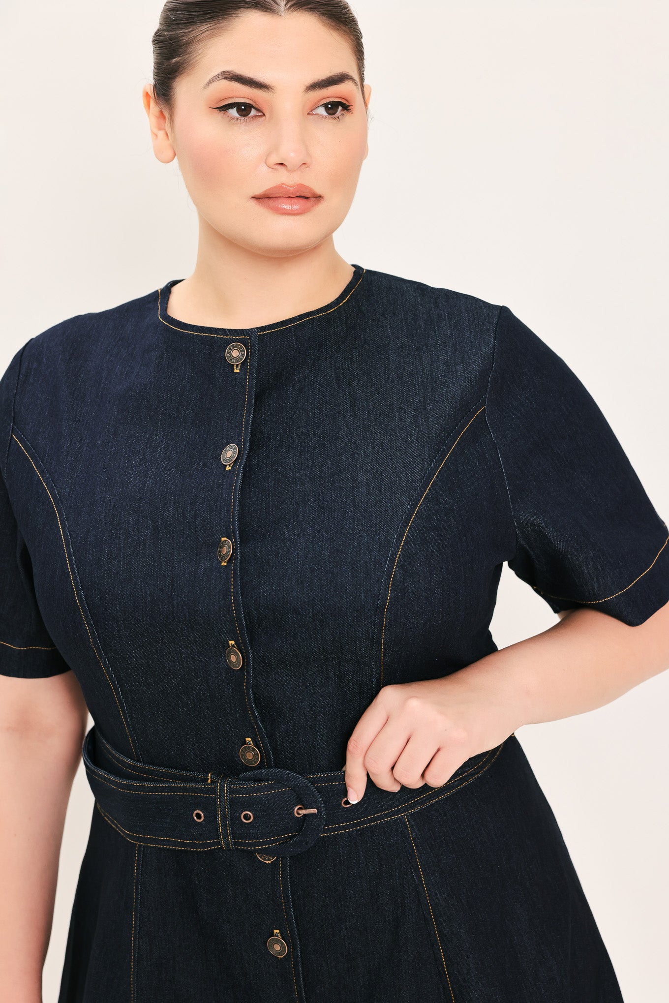 A woman modeling a dark indigo denim midi dress with short sleeves, a button-down front, and a matching belt with a metal buckle | Plus Curve Flying Tomato
