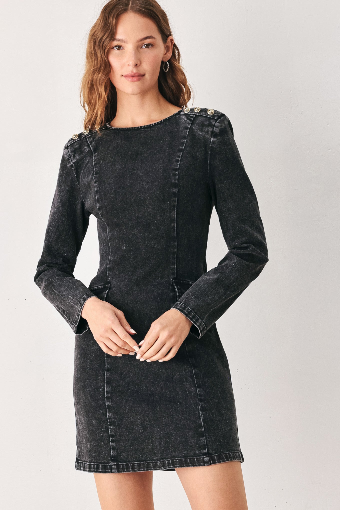 A woman wearing a dark black washed denim mini dress with shoulder embellishments and front patch pockets | FREEMARKET