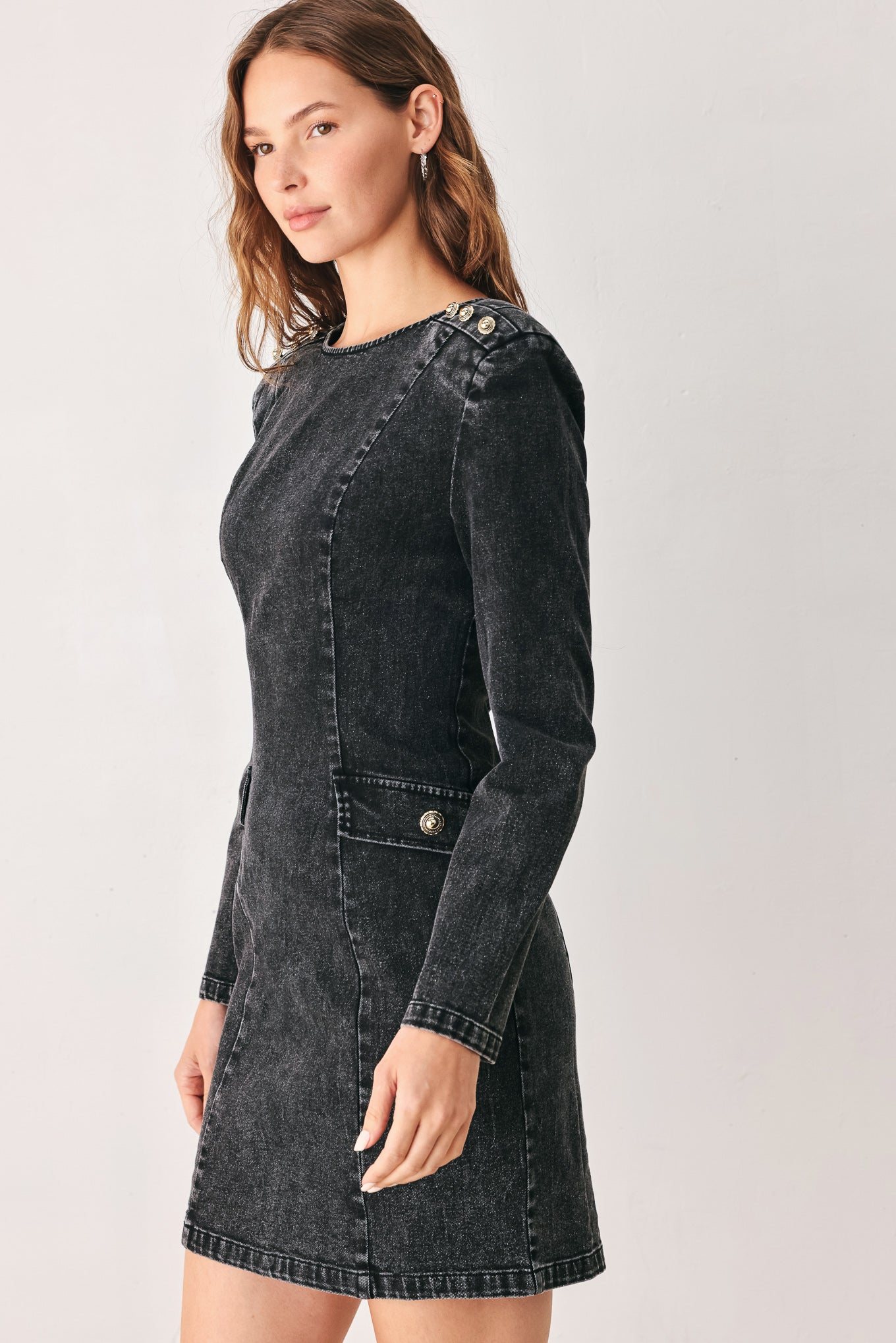 A woman wearing a dark black washed denim mini dress with shoulder embellishments and front patch pockets | FREEMARKET