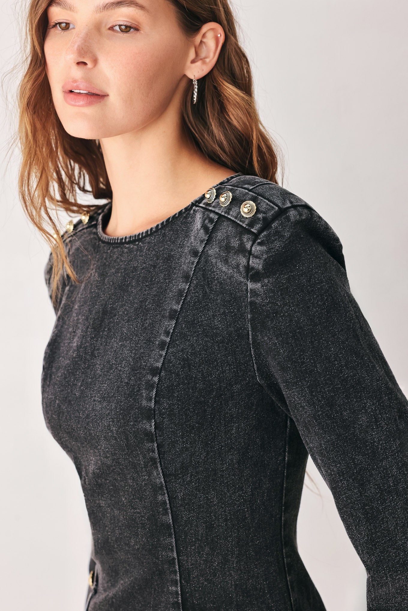 A woman wearing a dark black washed denim mini dress with shoulder embellishments and front patch pockets | FREEMARKET