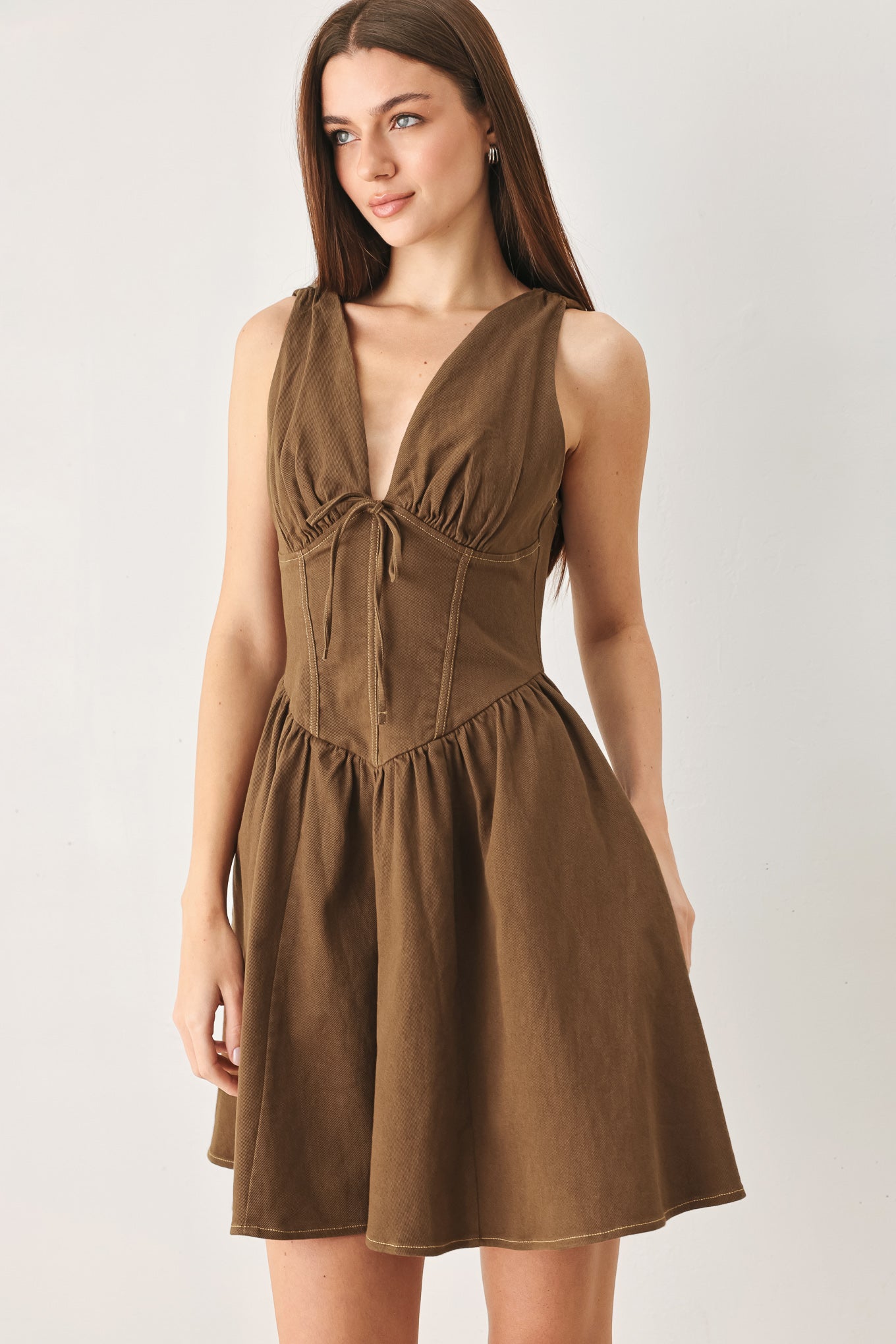 Woman wearing a washed brown woven mini dress featuring V neckline with tie, sleeveless, corset waist, full skirt and back zipper closure | FREEMARKET