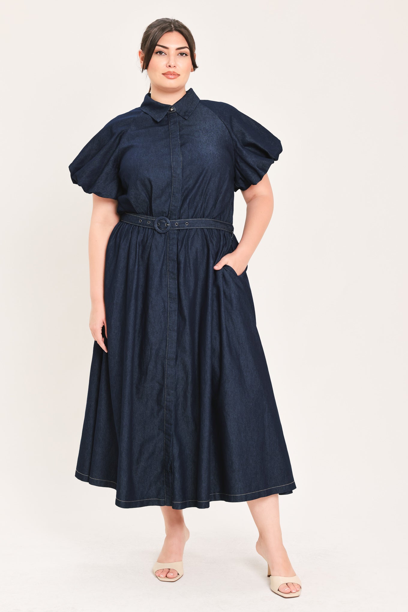 A woman models a dark indigo denim midi shirt dress with short puff sleeves, a pointed collar, and a matching dark belt | FREEMARKET Curve