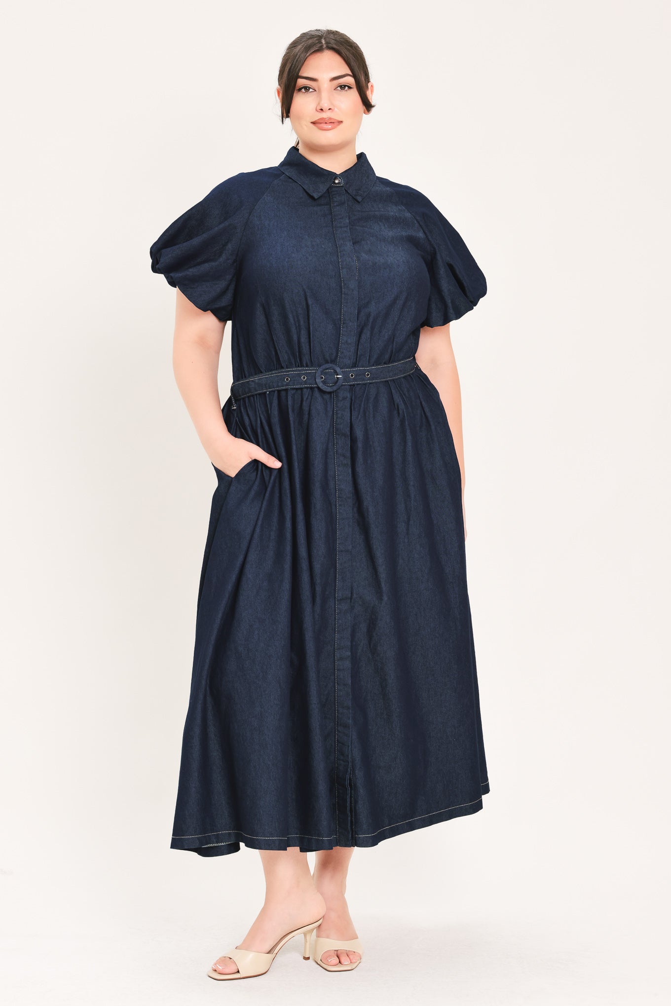 A woman models a dark indigo denim midi shirt dress with short puff sleeves, a pointed collar, and a matching dark belt | FREEMARKET Curve