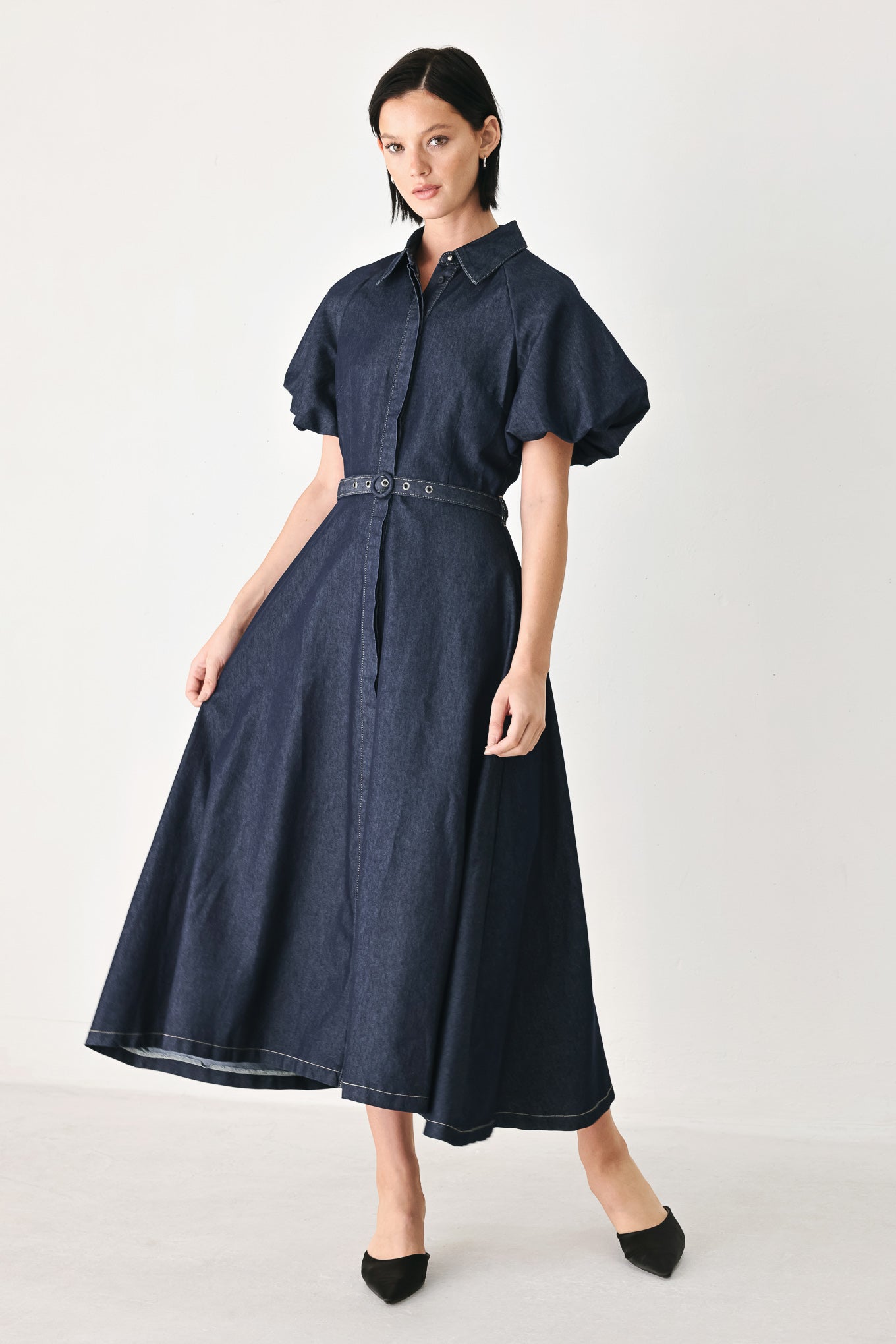 A woman models a dark indigo denim midi shirt dress with short puff sleeves, a pointed collar, and a matching dark belt | FREEMARKET
