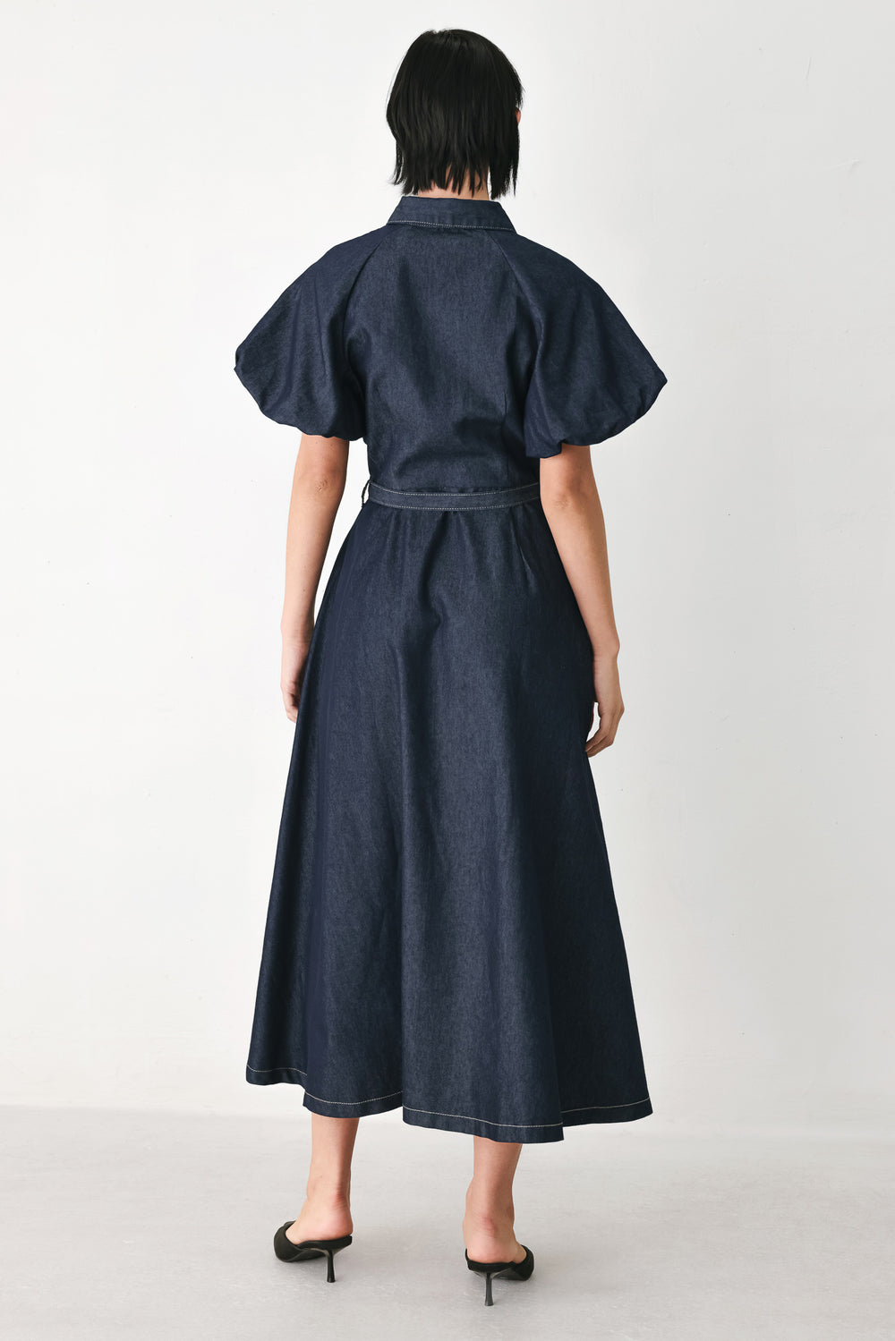 A woman models a dark indigo denim midi shirt dress with short puff sleeves, a pointed collar, and a matching dark belt | FREEMARKET