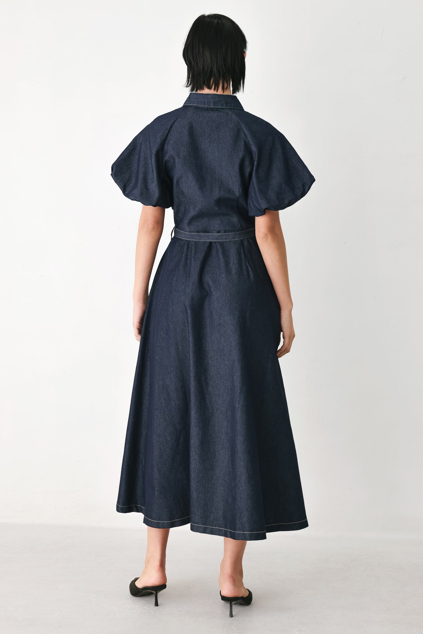 A woman models a dark indigo denim midi shirt dress with short puff sleeves, a pointed collar, and a matching dark belt | FREEMARKET