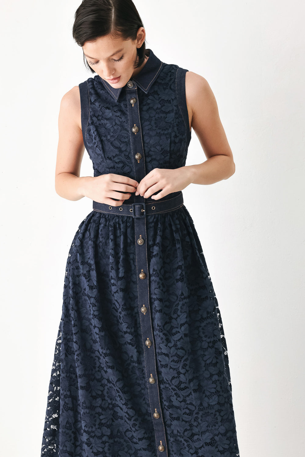 A woman modeling a sleeveless navy midi dress with a lace overlay, button-front bodice, and matching belt | FREEMARKET
