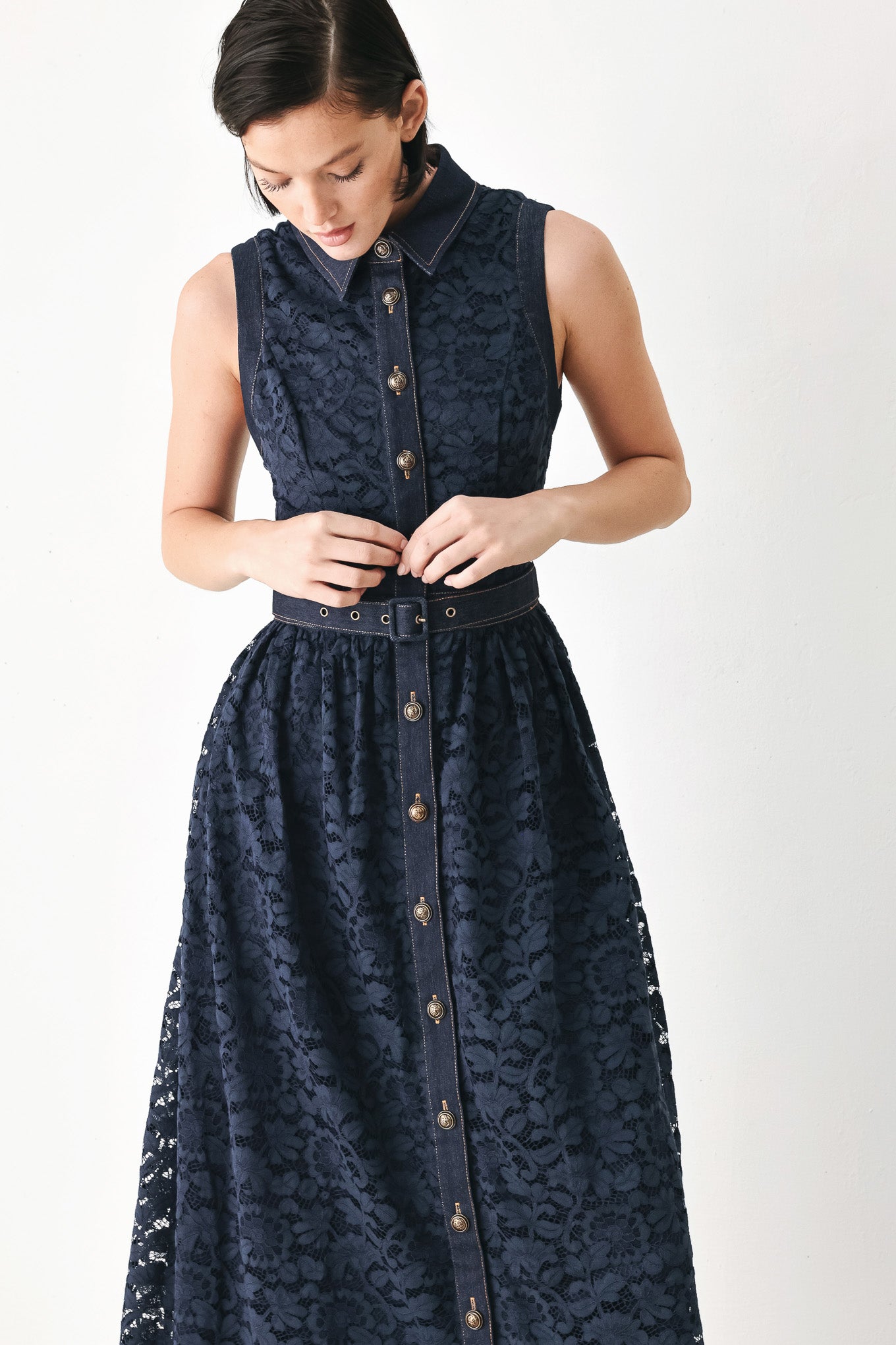 A woman modeling a sleeveless navy midi dress with a lace overlay, button-front bodice, and matching belt | FREEMARKET