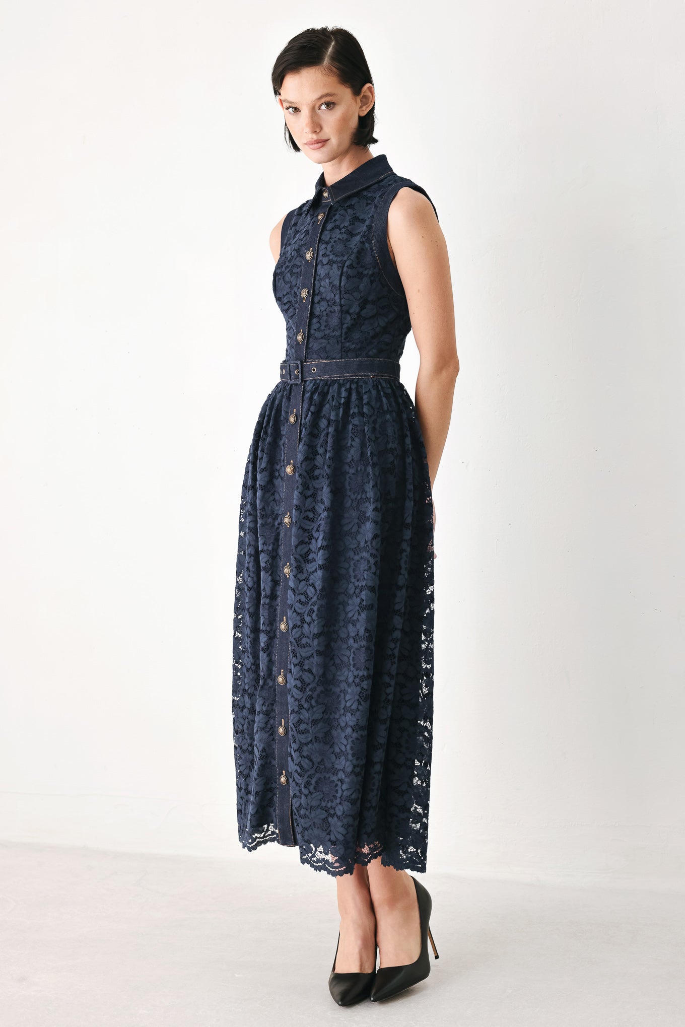 A woman modeling a sleeveless navy midi dress with a lace overlay, button-front bodice, and matching belt | FREEMARKET