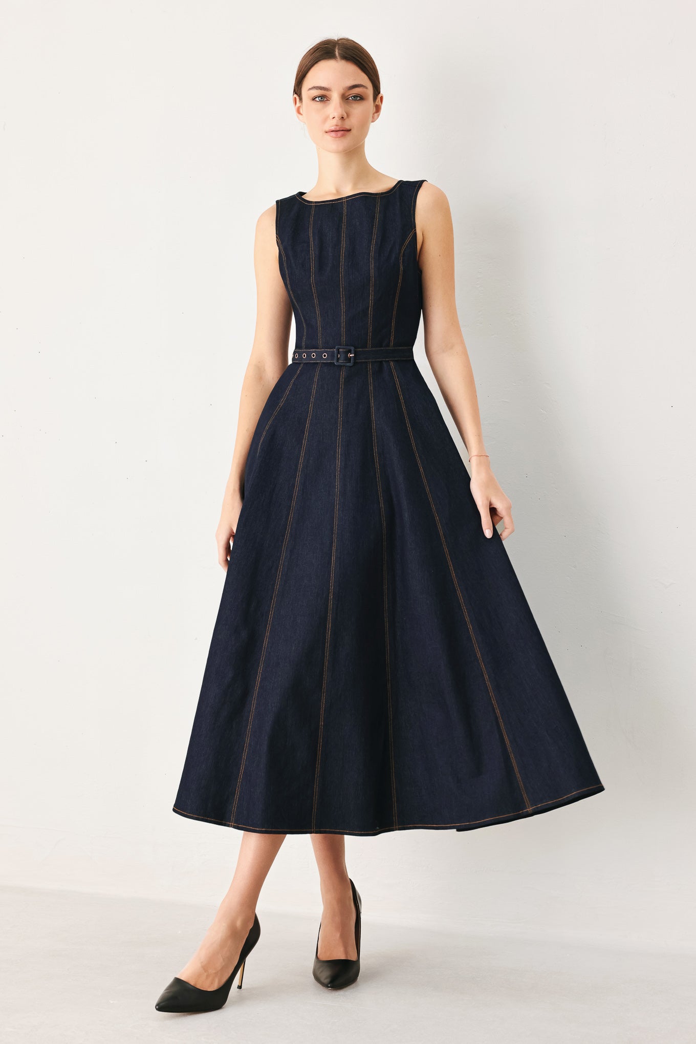 Woman wearing a dark denim sleeveless midi dress featuring wide neckline, self belt, full circle skirt and back zipper closure | FREEMARKET