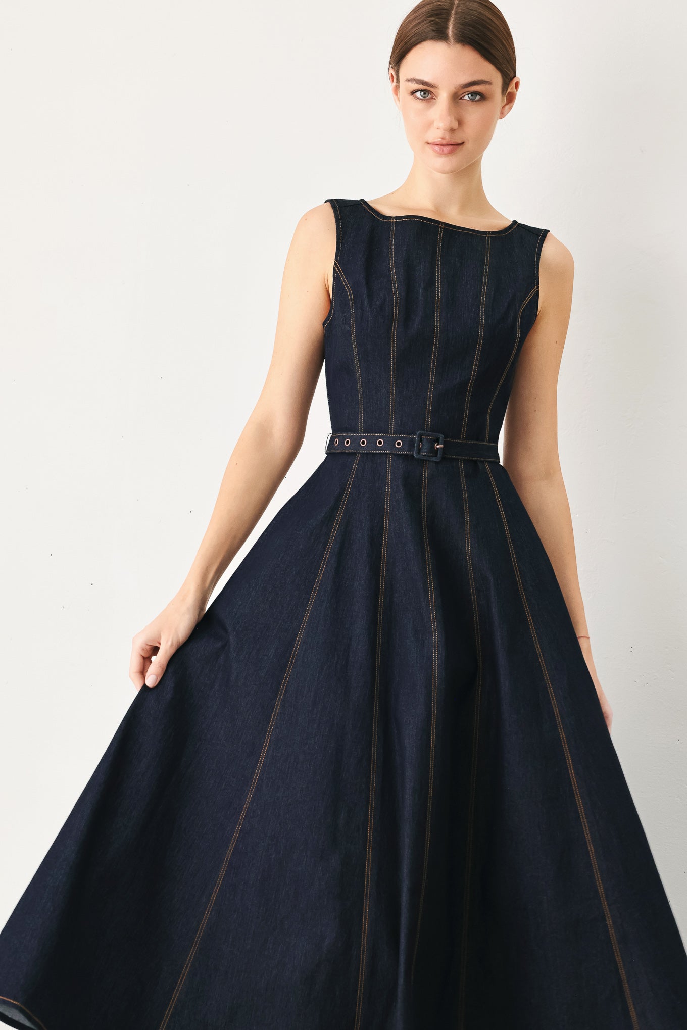 Woman wearing a dark denim sleeveless midi dress featuring wide neckline, self belt, full circle skirt and back zipper closure | FREEMARKET