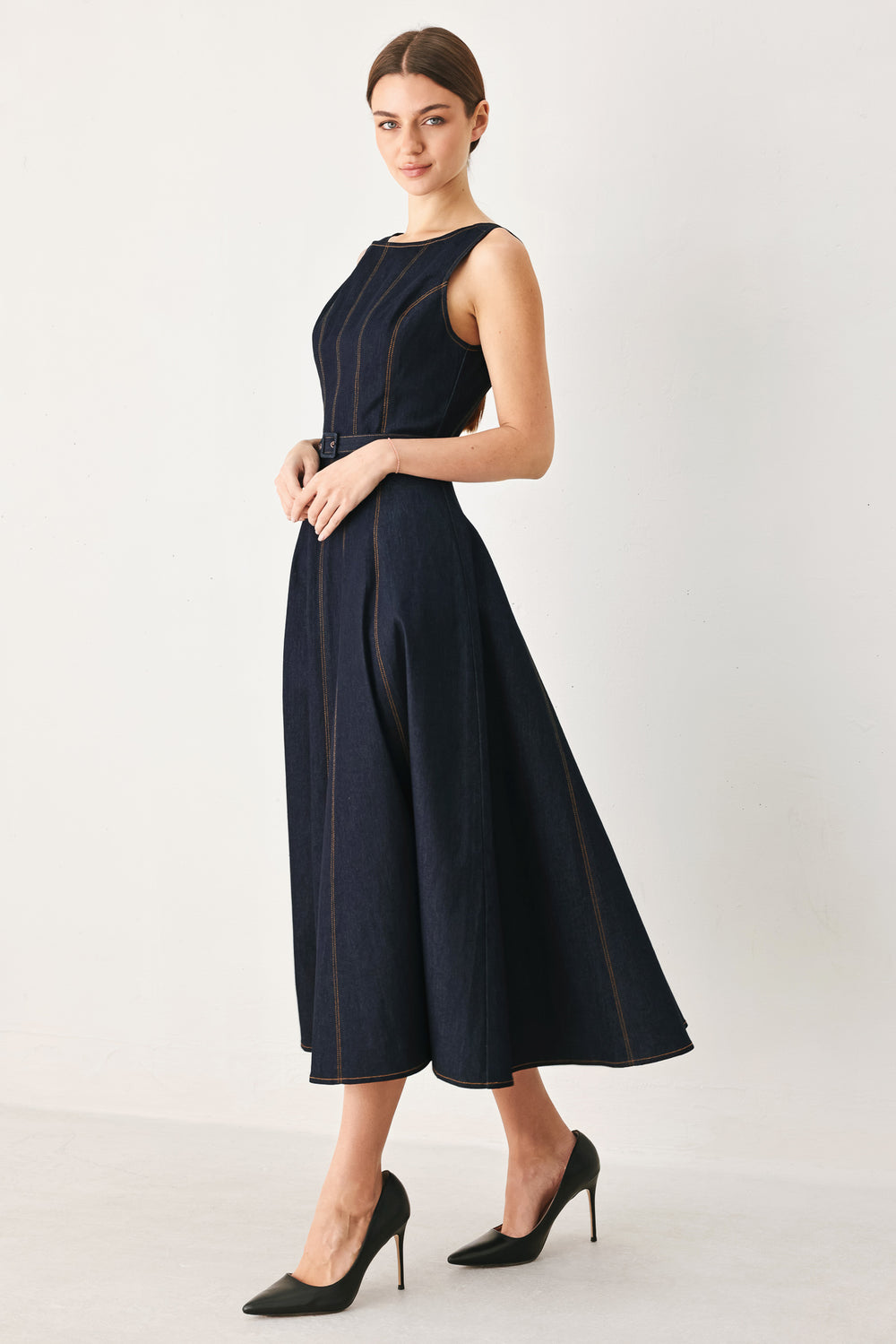Woman wearing a dark denim sleeveless midi dress featuring wide neckline, self belt, full circle skirt and back zipper closure | FREEMARKET