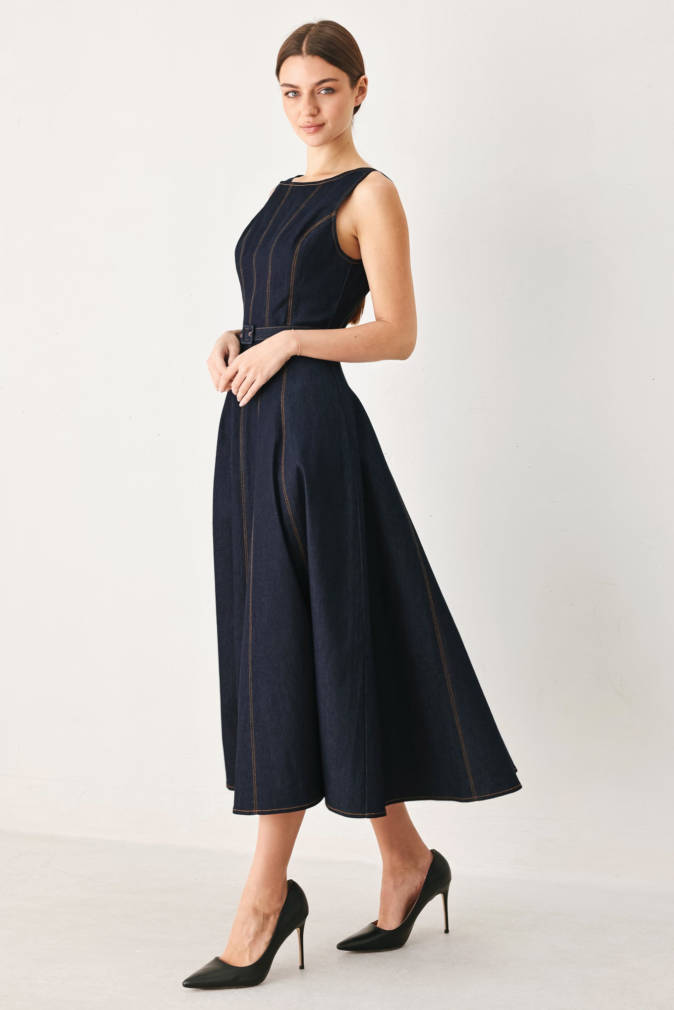 Woman wearing a dark denim sleeveless midi dress featuring wide neckline, self belt, full circle skirt and back zipper closure | FREEMARKET