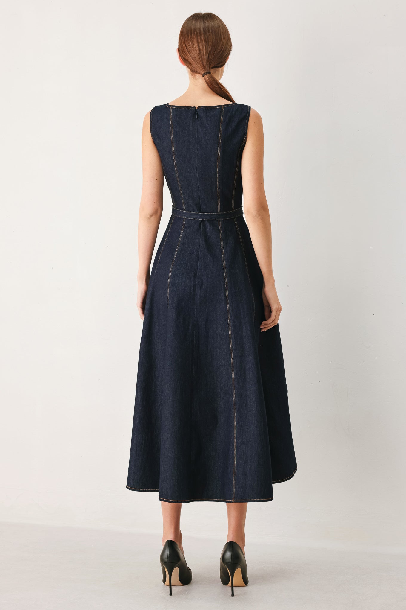 Woman wearing a dark denim sleeveless midi dress featuring wide neckline, self belt, full circle skirt and back zipper closure | FREEMARKET