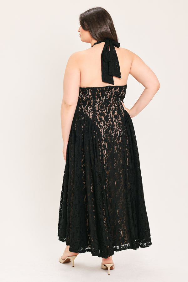 A woman modeling a sleeveless black lace halter maxi dress with a deep V-neckline, holding a small black handbag against a plain light background | FREEMARKET Curve