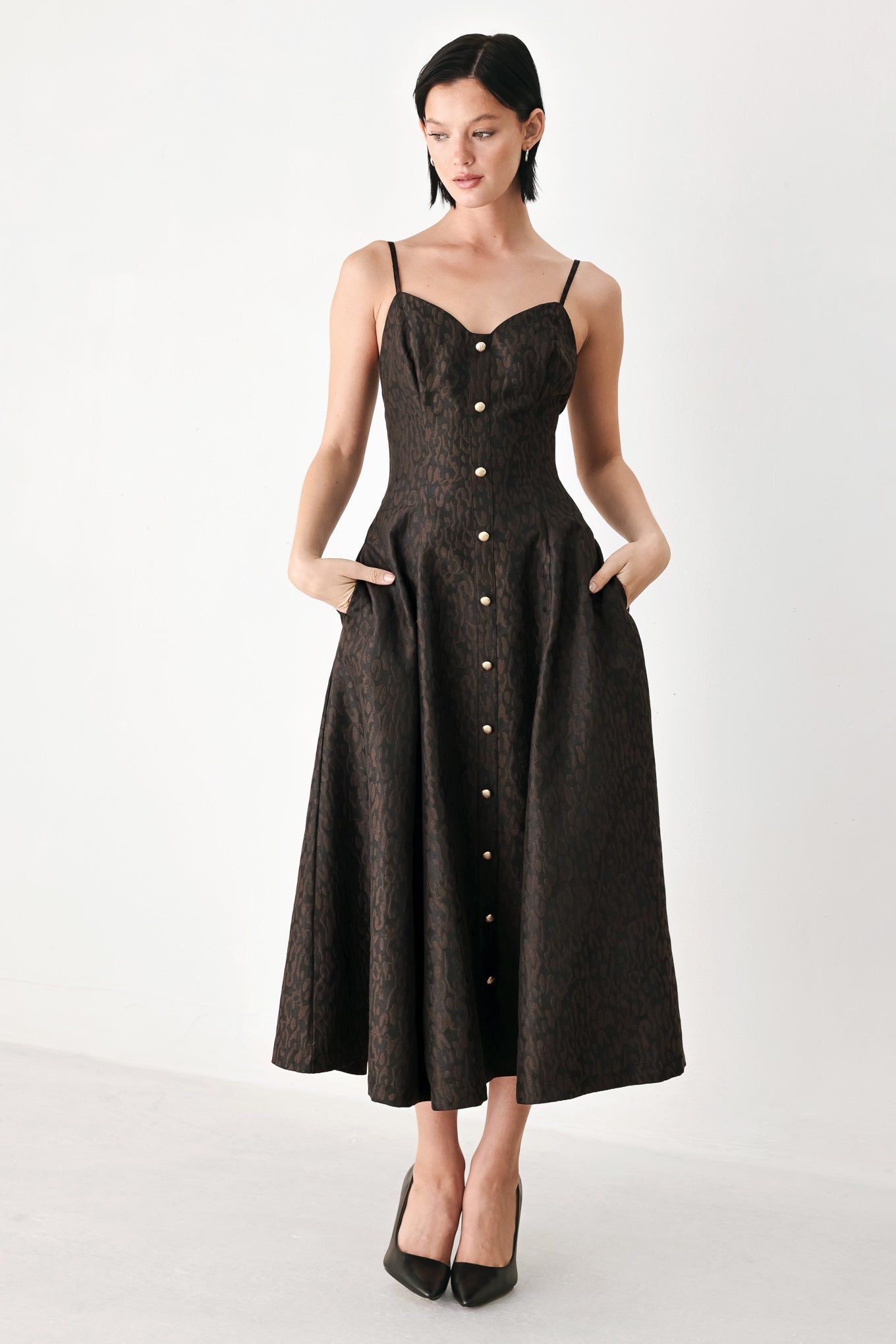 A woman modeling a black midi dress with a textured jacquard leopard pattern, featuring thin spaghetti straps, a sweetheart neckline, a button-down front, and side pockets | FREEMARKET