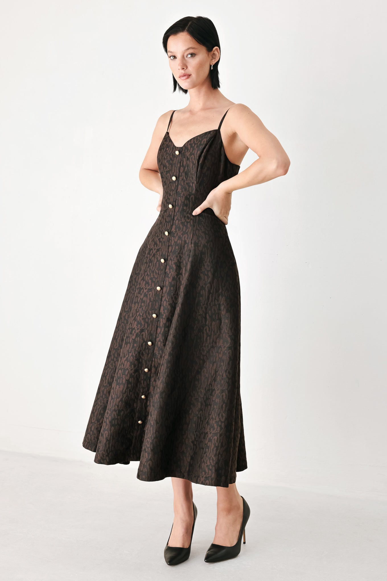 A woman modeling a black midi dress with a textured jacquard leopard pattern, featuring thin spaghetti straps, a sweetheart neckline, a button-down front, and side pockets | FREEMARKET