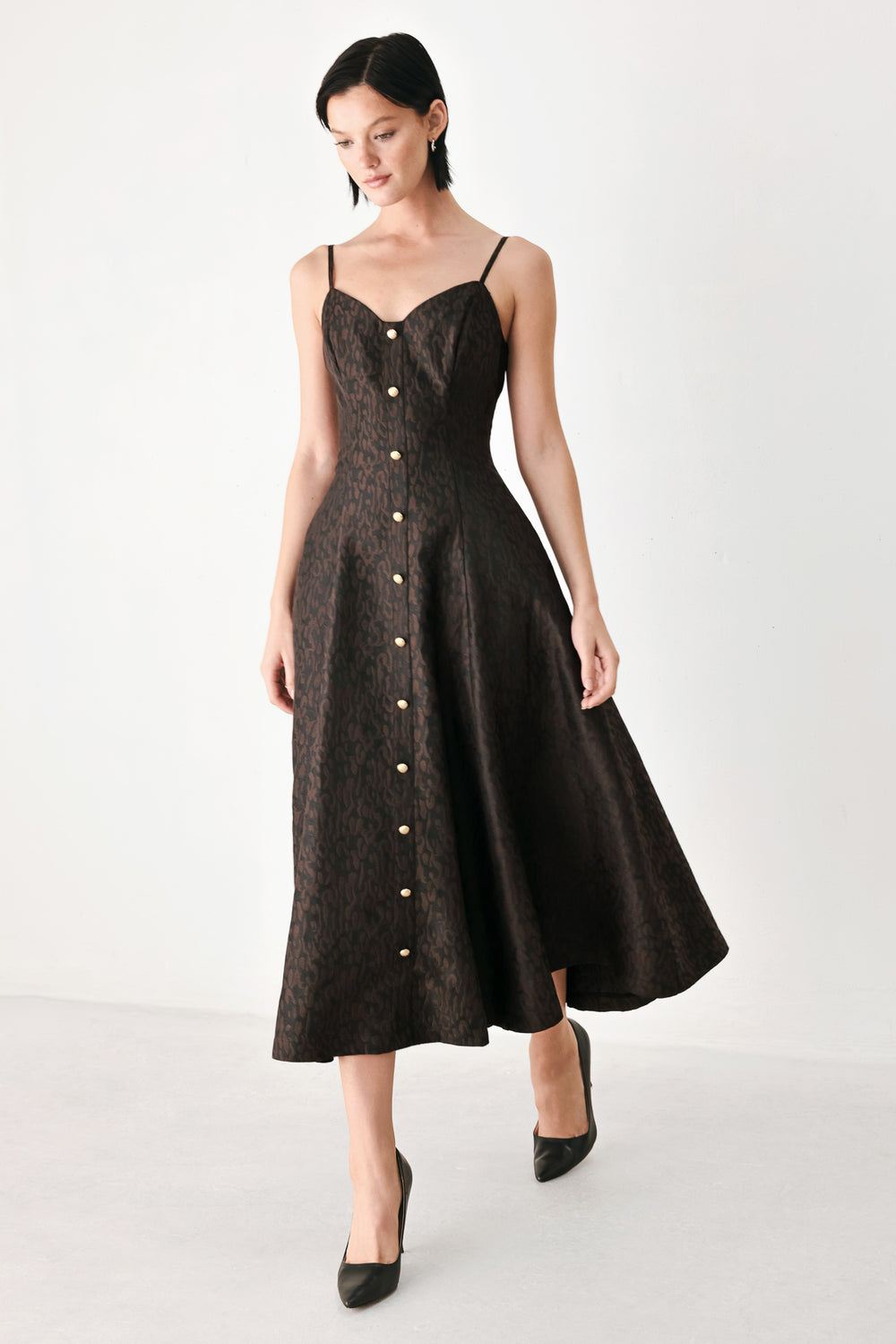 A woman modeling a black midi dress with a textured jacquard leopard pattern, featuring thin spaghetti straps, a sweetheart neckline, a button-down front, and side pockets | FREEMARKET