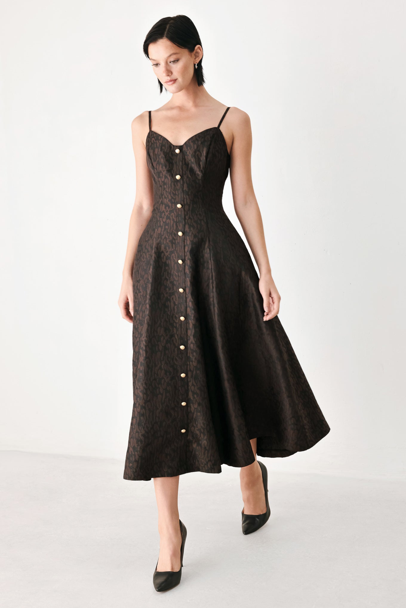 A woman modeling a black midi dress with a textured jacquard leopard pattern, featuring thin spaghetti straps, a sweetheart neckline, a button-down front, and side pockets | FREEMARKET