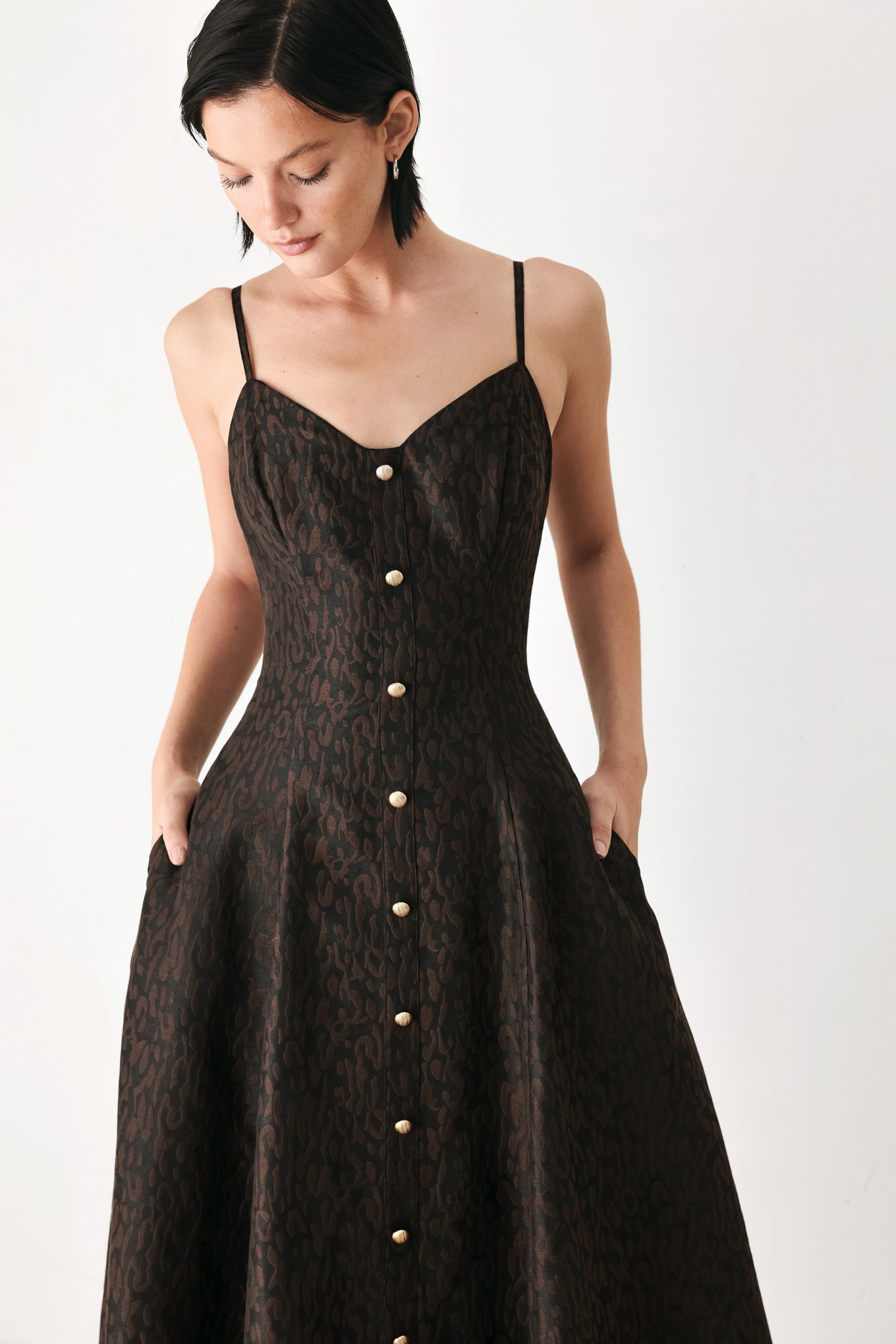 A woman modeling a black midi dress with a textured jacquard leopard pattern, featuring thin spaghetti straps, a sweetheart neckline, a button-down front, and side pockets | FREEMARKET
