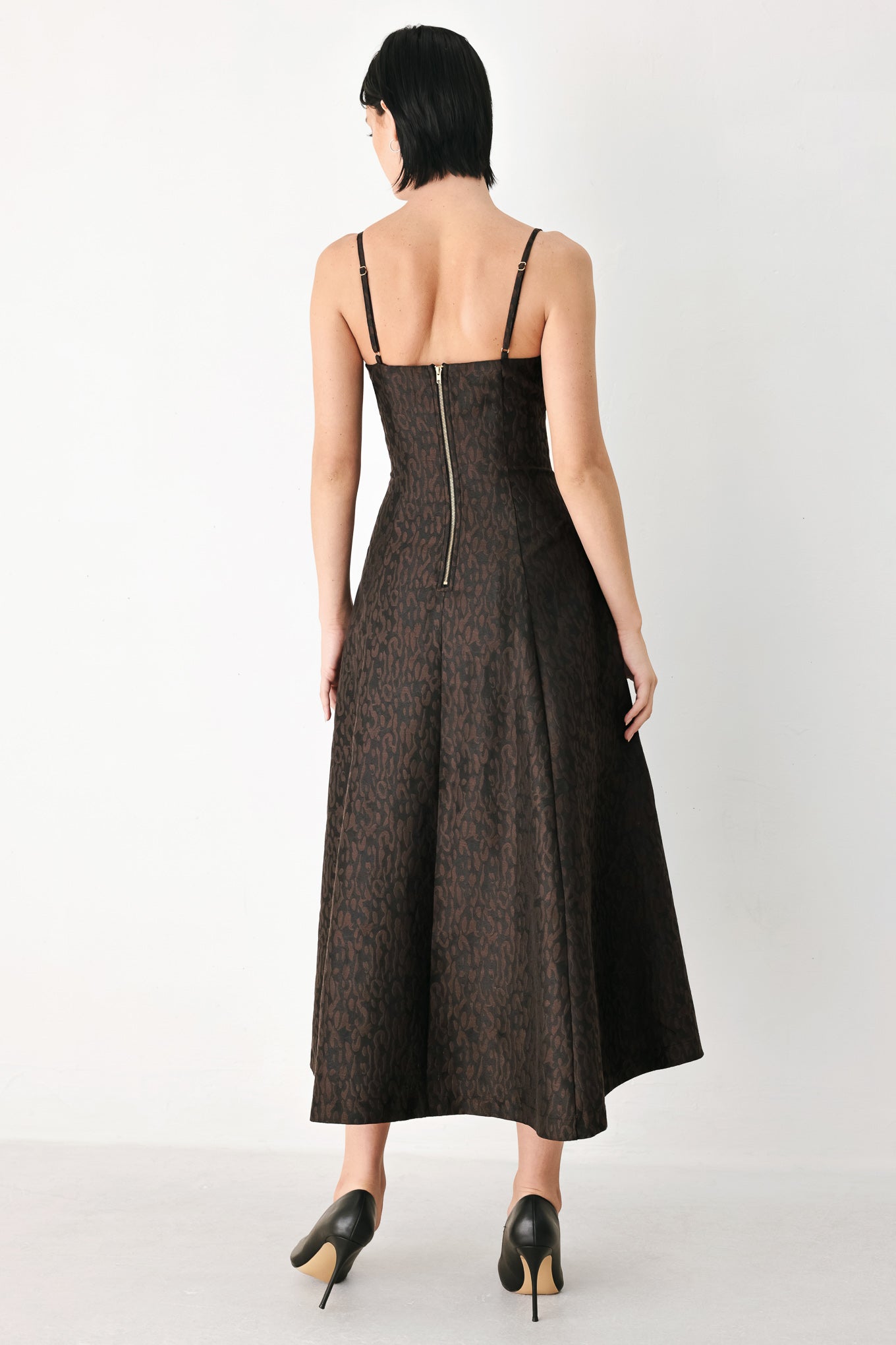 A woman modeling a black midi dress with a textured jacquard leopard pattern, featuring thin spaghetti straps, a sweetheart neckline, a button-down front, and side pockets | FREEMARKET