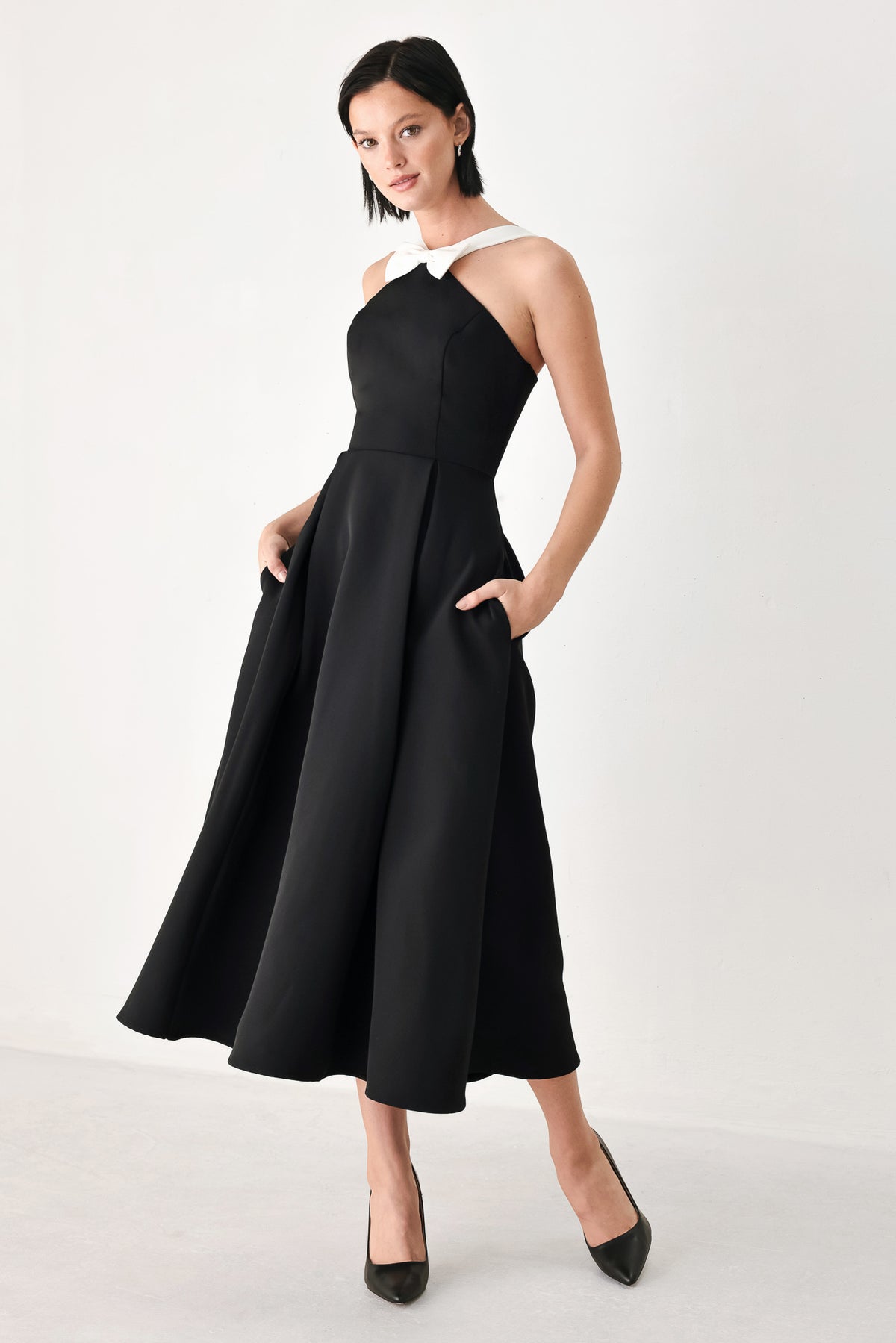 A woman modeling a black halter midi dress with a contrasting white bow at the neckline | FREEMARKET