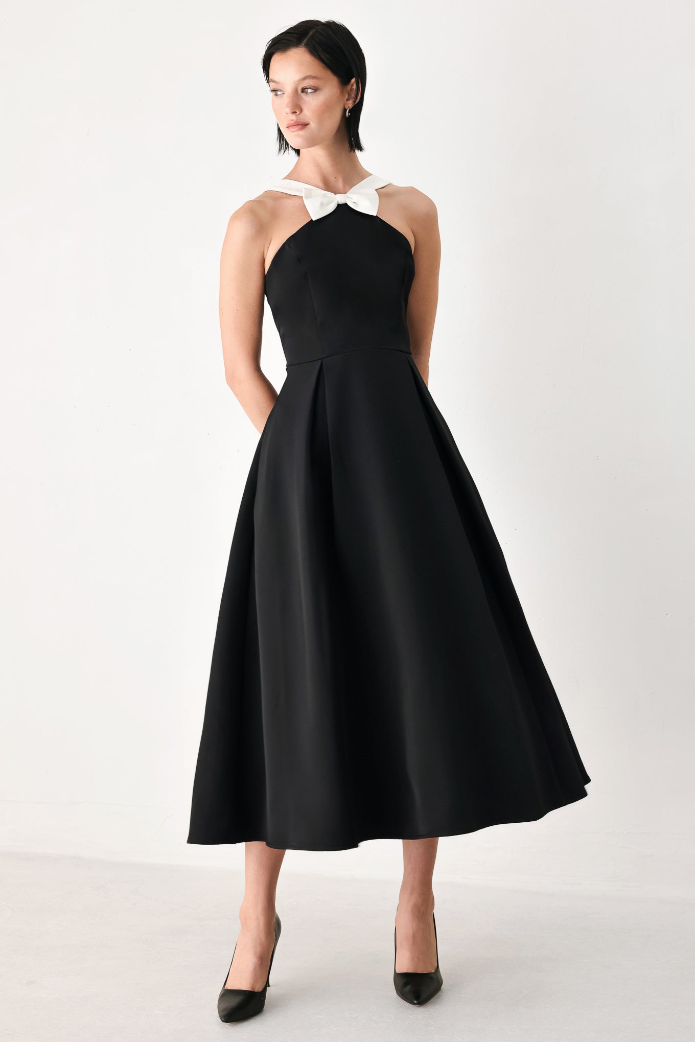 A woman modeling a black halter midi dress with a contrasting white bow at the neckline | FREEMARKET