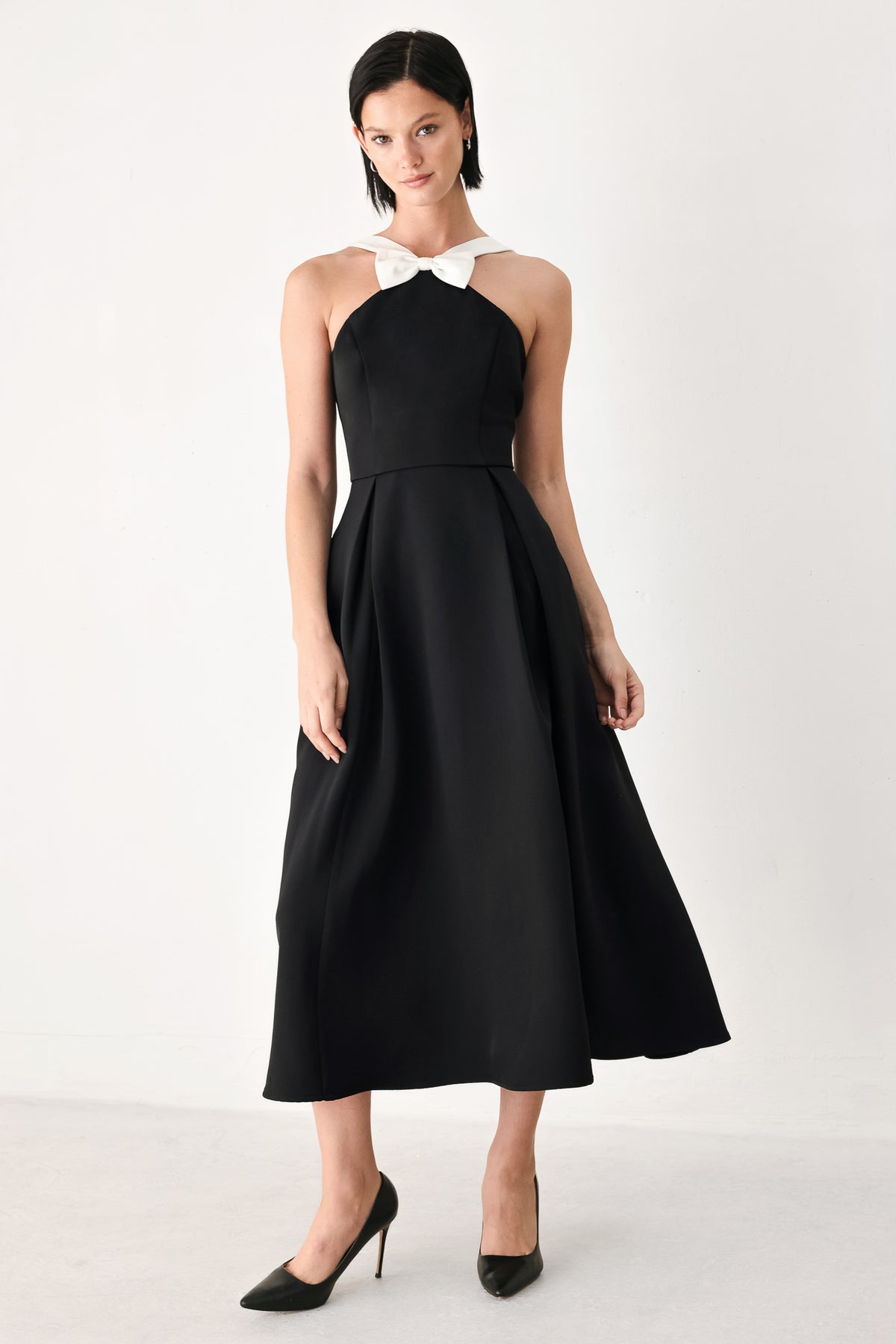 A woman modeling a black halter midi dress with a contrasting white bow at the neckline | FREEMARKET